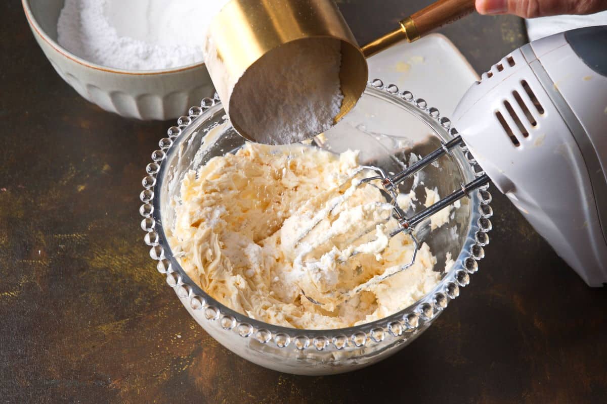 Softened butter and powdered sugar in a mixing bowl with a hand mixer resting nearby on a kitchen counter