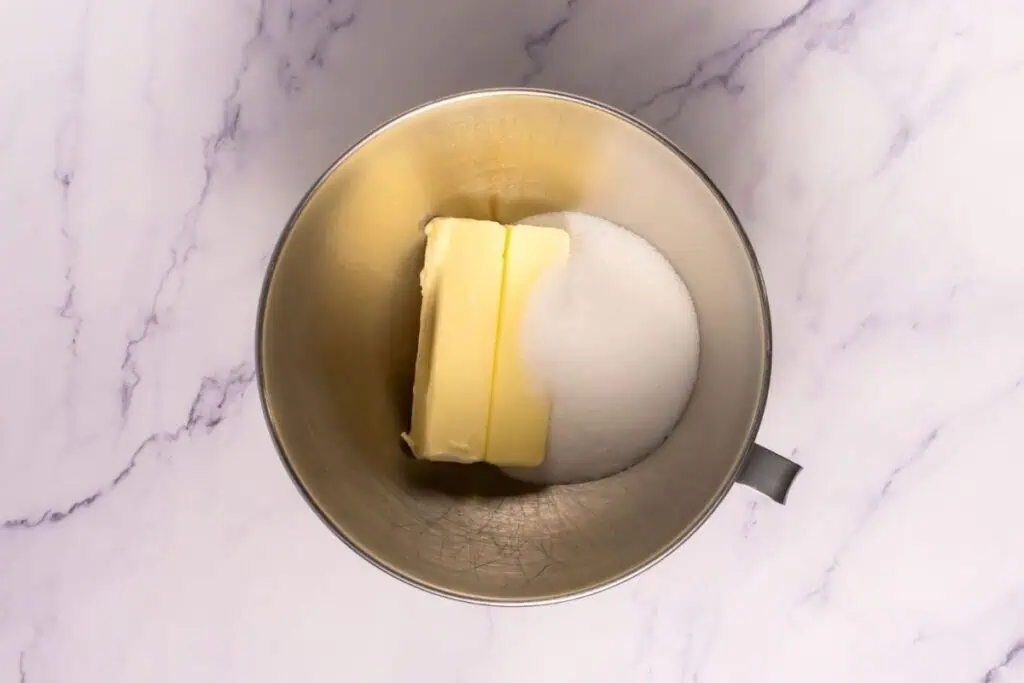 Softened unsalted butter in a stainless steel mixing bowl on a kitchen counter with a wooden spoon nearby