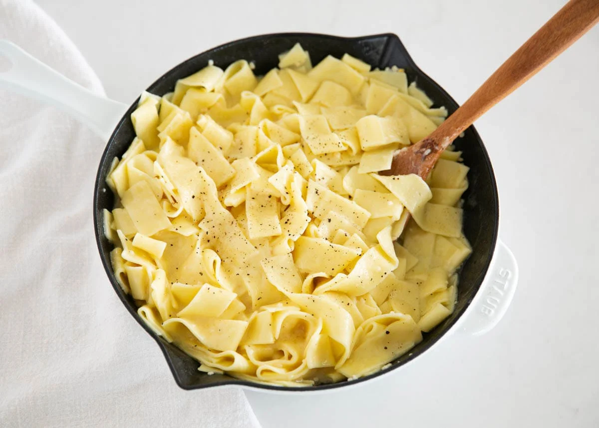 Spaghetti being tossed in a skillet with a glossy garlic butter sauce on a home stove, steam rising