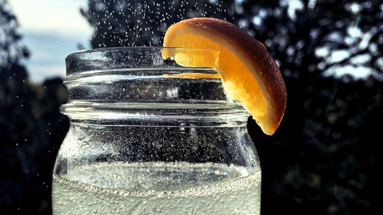 Sparkling water being poured into an iced green lime and mint mocktail in a glass on a kitchen counter