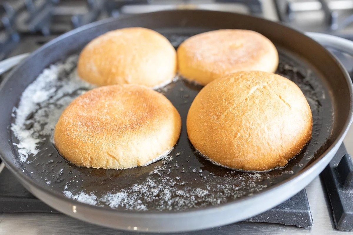 Split sandwich buns toasting cut-side down in a skillet on a stovetop