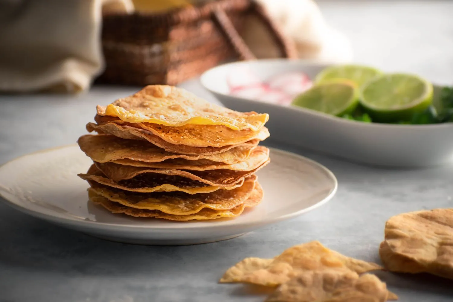 Stack of tostada shells next to large flour tortillas on a clean kitchen counter with warm lighting