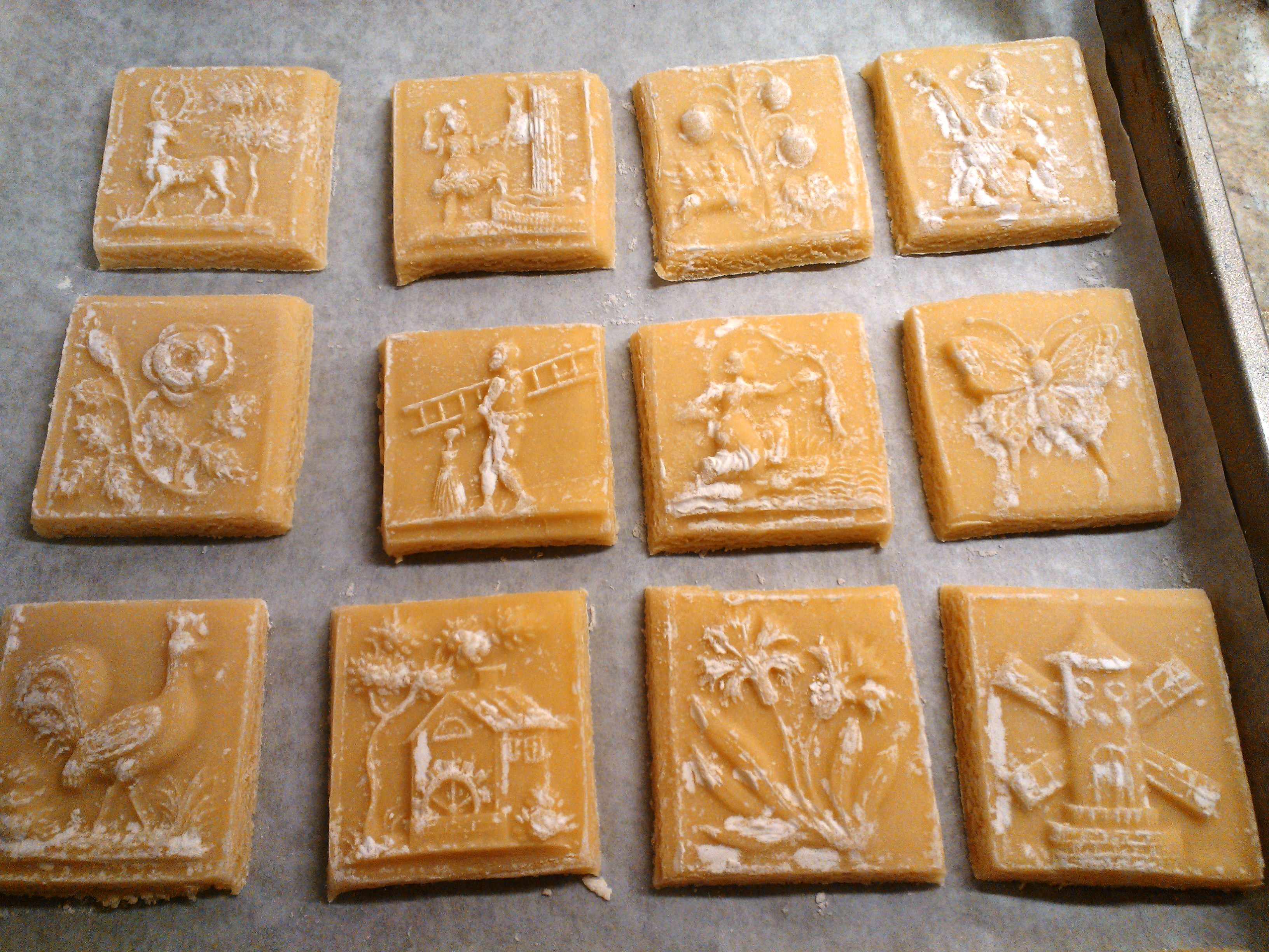 Stamped Springerle cookies spaced on a parchment-lined baking sheet, sitting uncovered on a kitchen counter to dry with a clean towel nearby