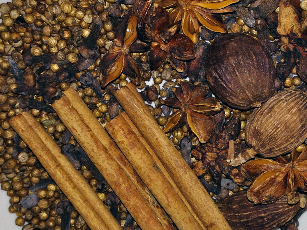 Star anise, cinnamon stick, cloves, coriander seeds, and fennel seeds toasting in a small skillet on a stove