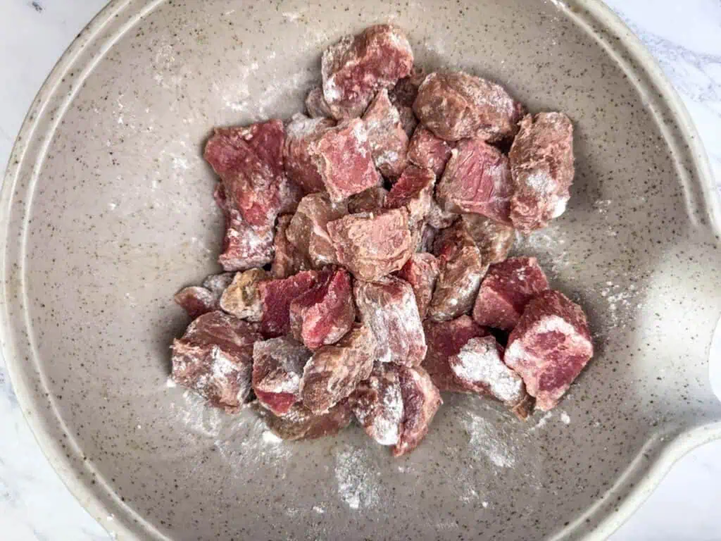 Stew beef cubes lightly coated in flour in a mixing bowl on a kitchen counter, ready to be browned
