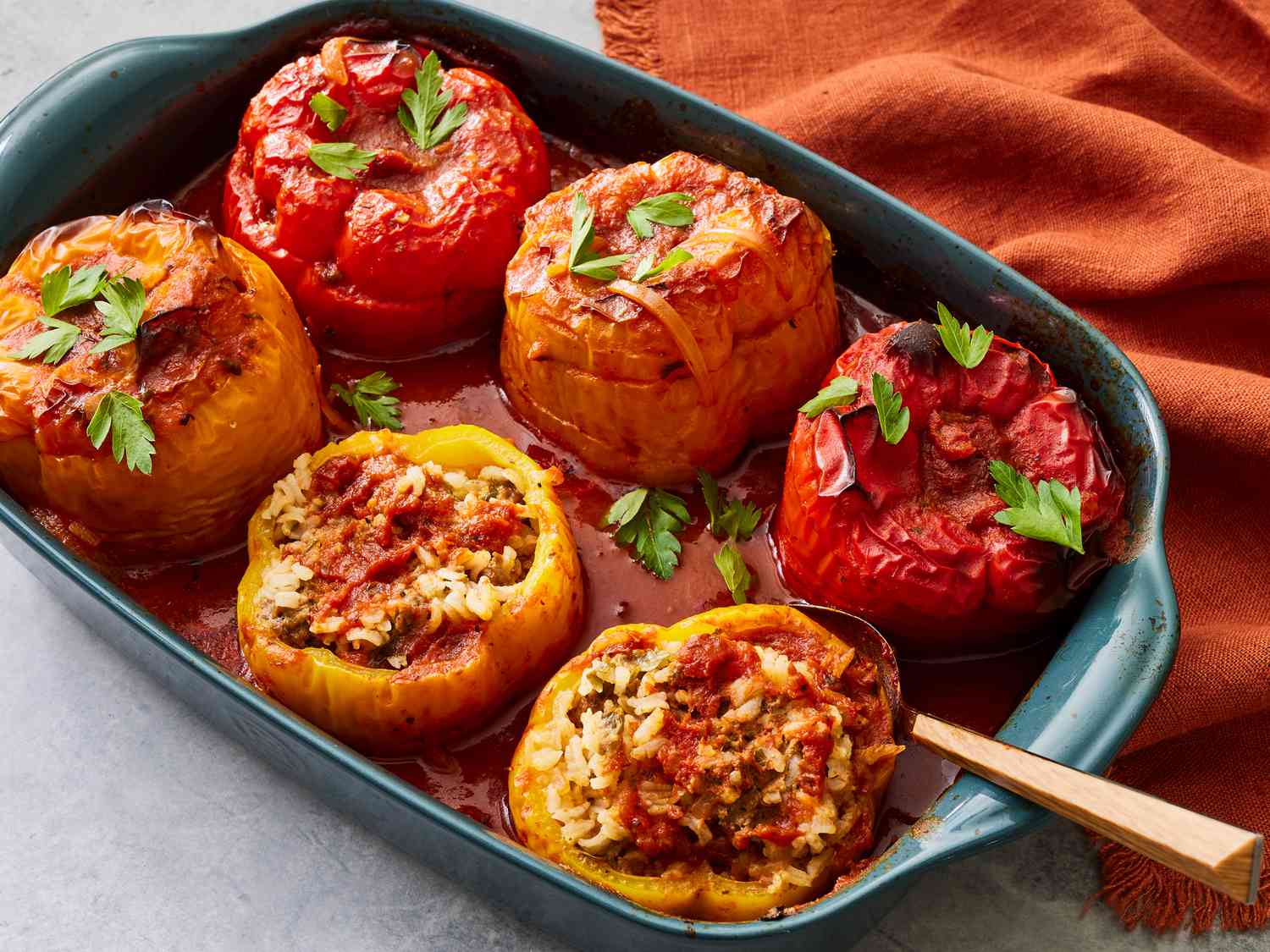 Stuffed green peppers arranged upright in a baking dish with tomato sauce before going into the oven
