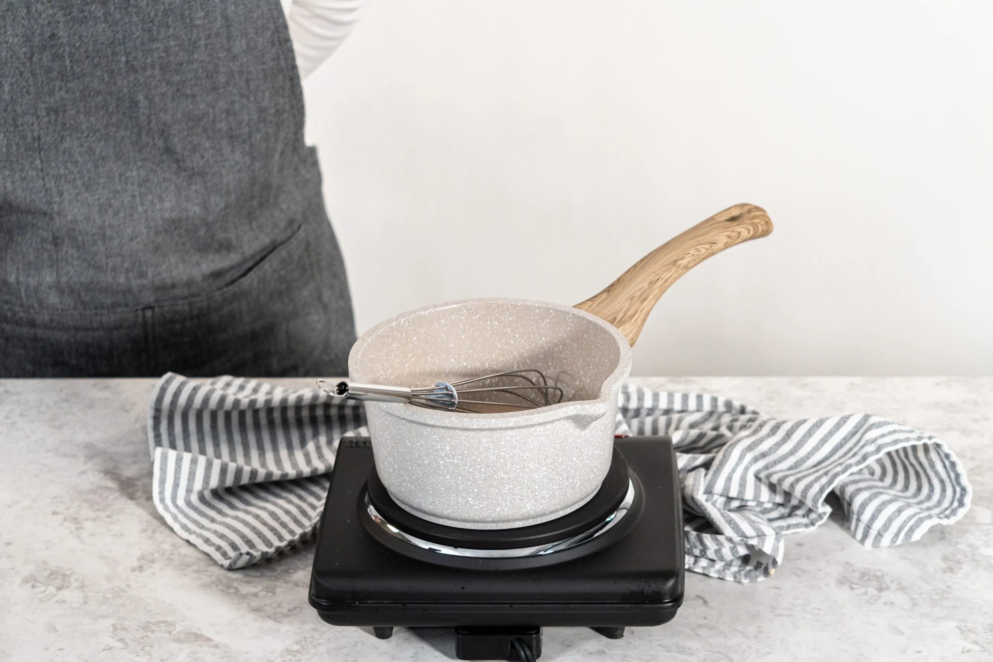 Sugar and water being stirred in a small saucepan on a stovetop until fully dissolved with gentle steam rising