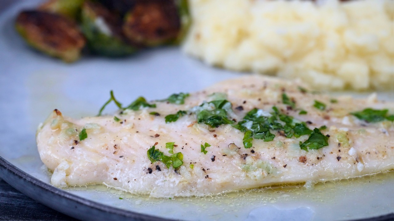 Swai fillets, lemon, butter, garlic, parsley, flour, and spices arranged on a clean kitchen counter with a skillet nearby