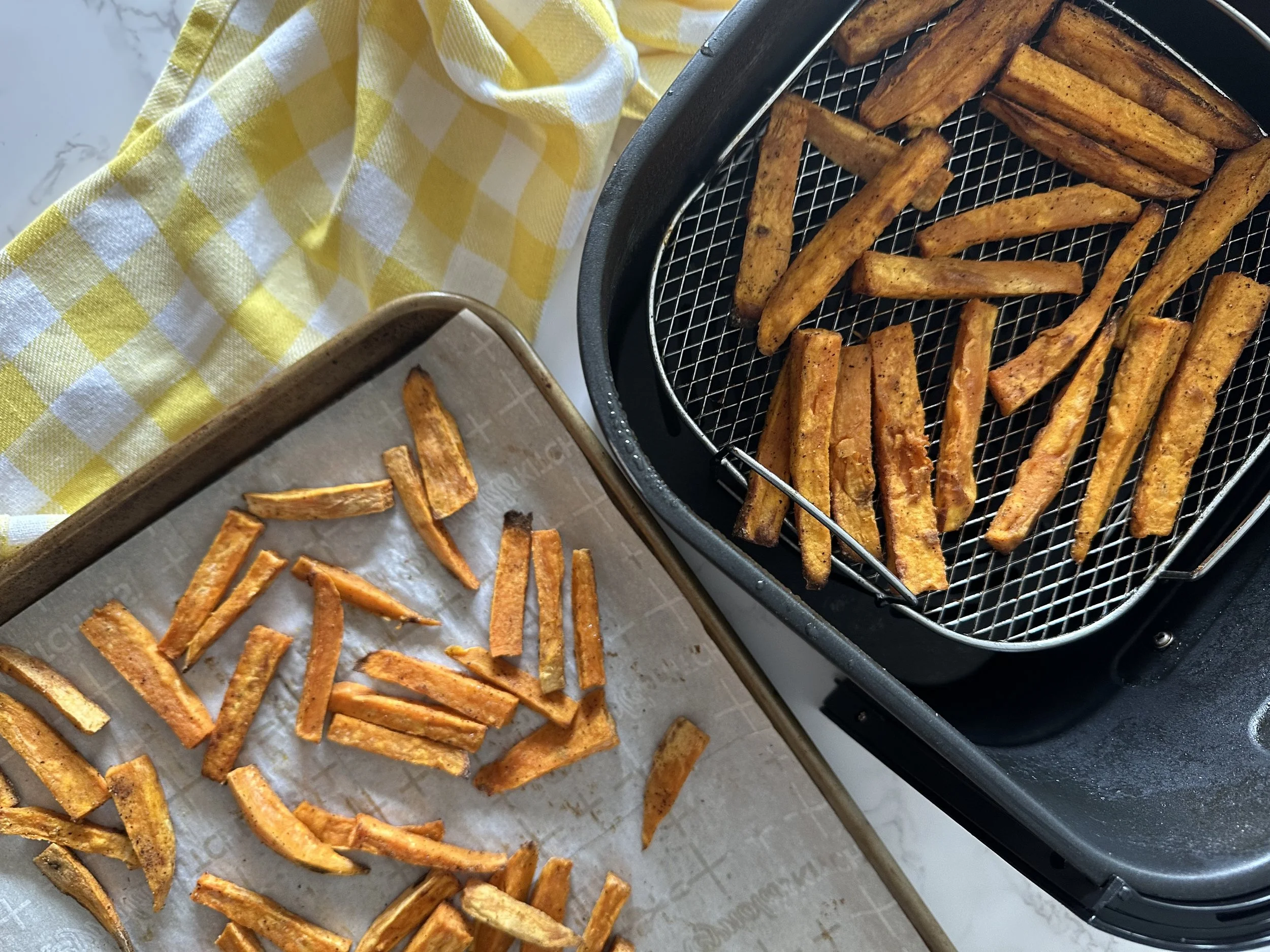 Sweet potato fries cooking in an air fryer basket mid-cook with browned edges beginning to form, shot over a clean kitchen counter