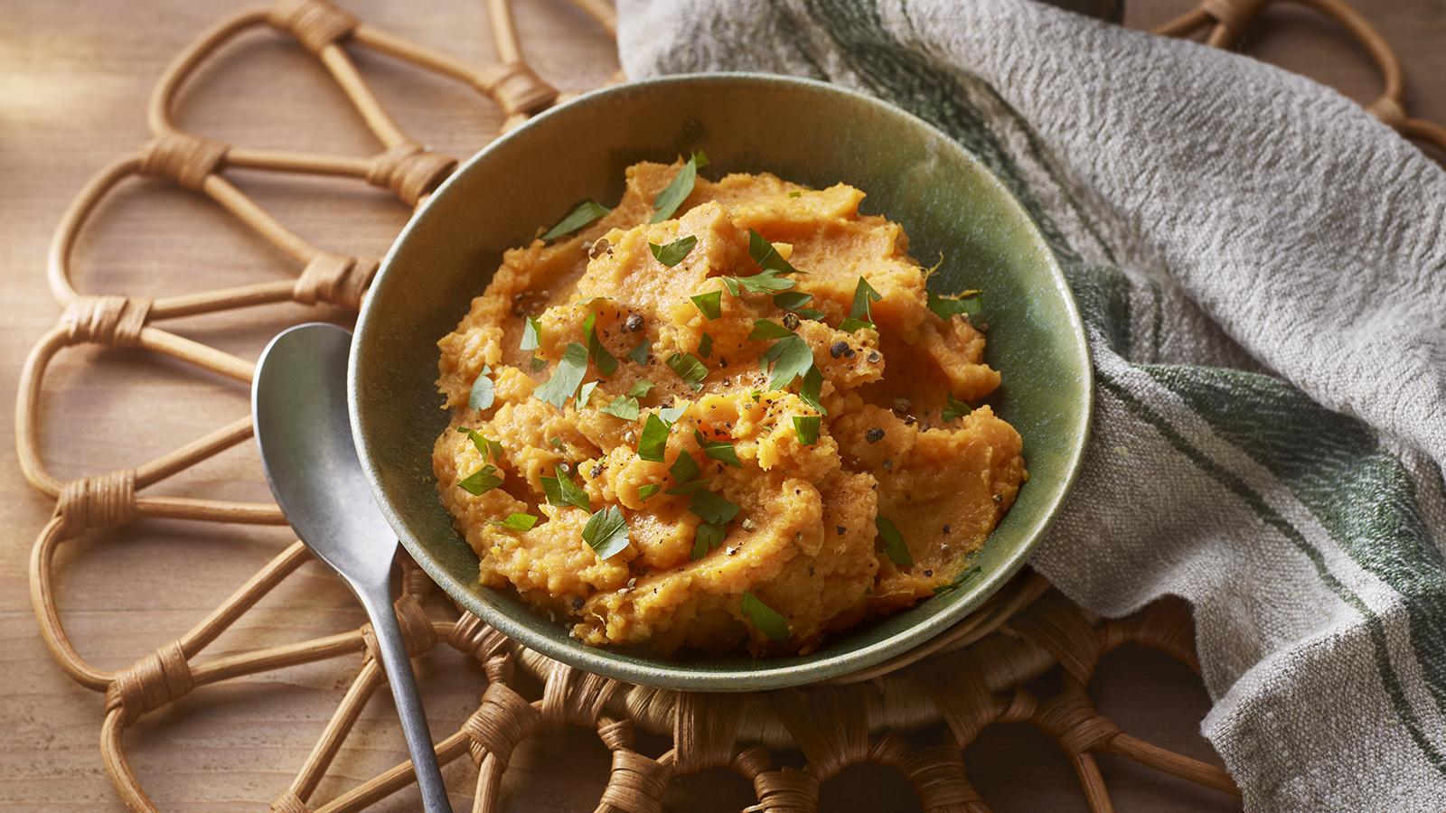Sweet potatoes, butter, milk, sour cream, salt, pepper, and spices arranged on a wooden cutting board on a kitchen counter