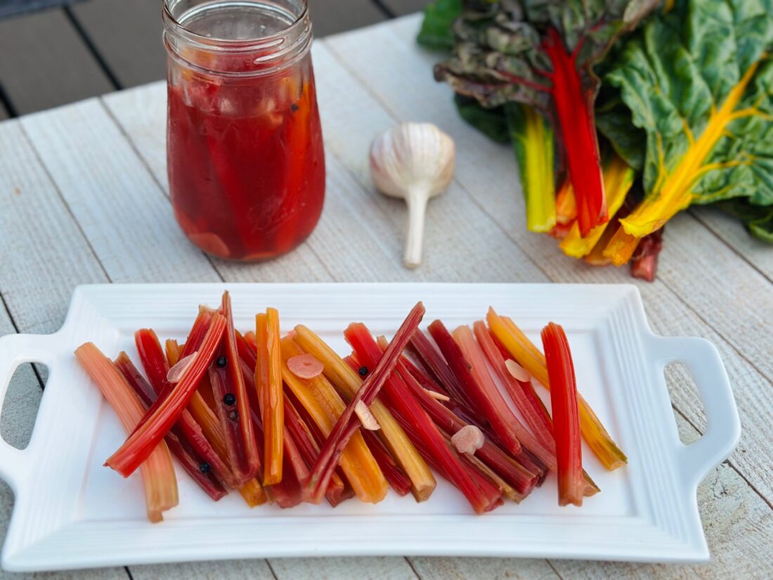 Swiss chard stems sliced into thin half-moons on a wooden cutting board with a chef's knife