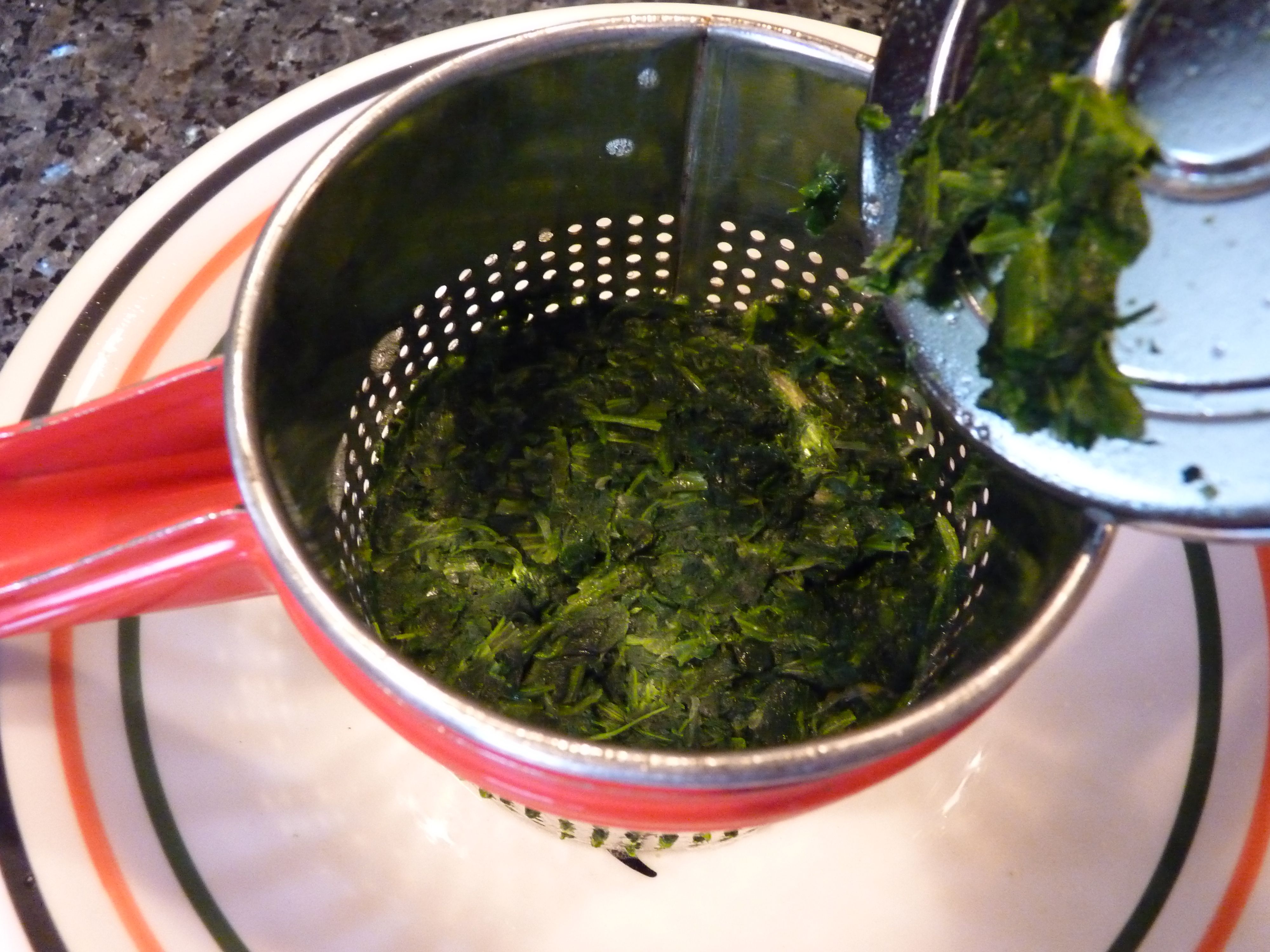 Thawed spinach being squeezed over a fine mesh strainer to remove excess water before adding to dip