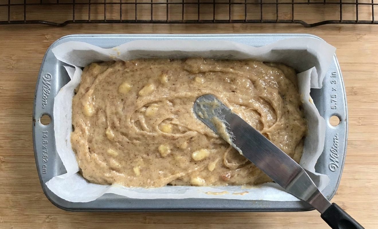 Thick banana bread batter smoothed into a parchment lined loaf pan before baking