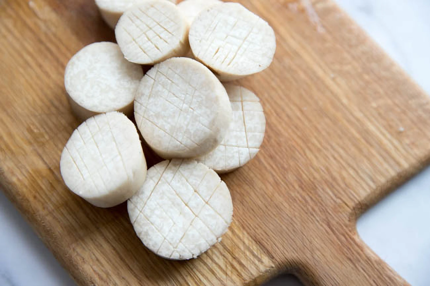 Thick coin slices of king oyster mushroom stems arranged in a single layer on a cutting board, with the mushroom caps set aside nearby