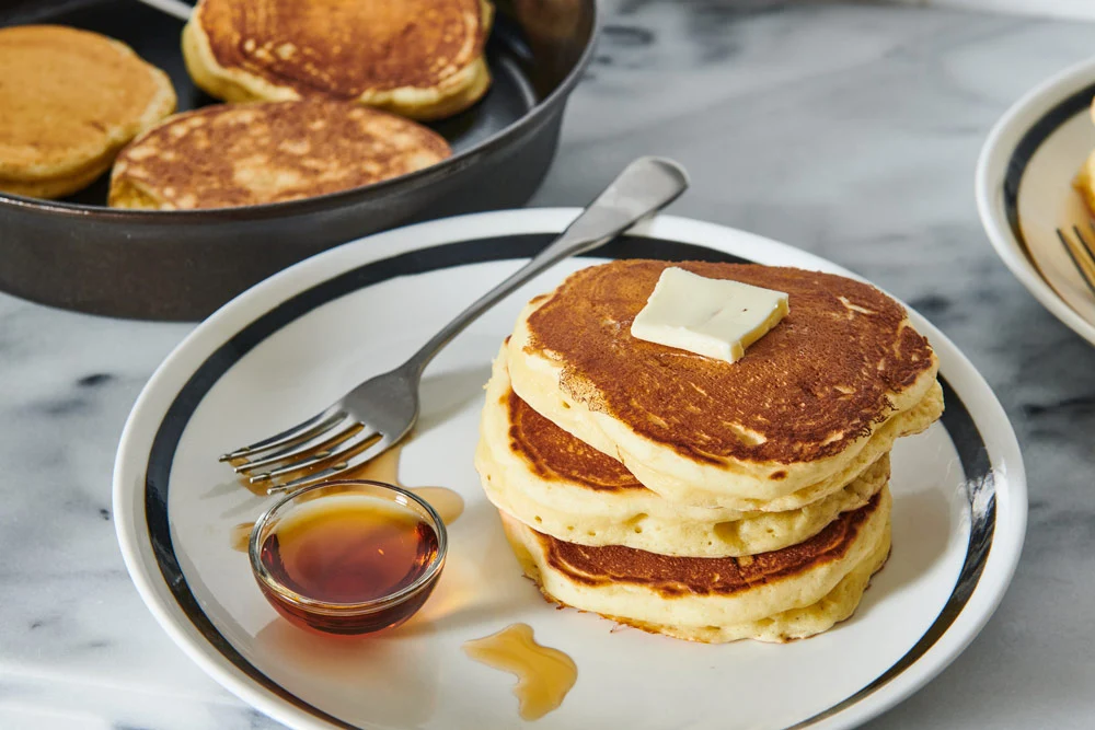 Thick pancake batter rounds cooking in a cast iron skillet on a stovetop with gentle bubbles forming on the surface
