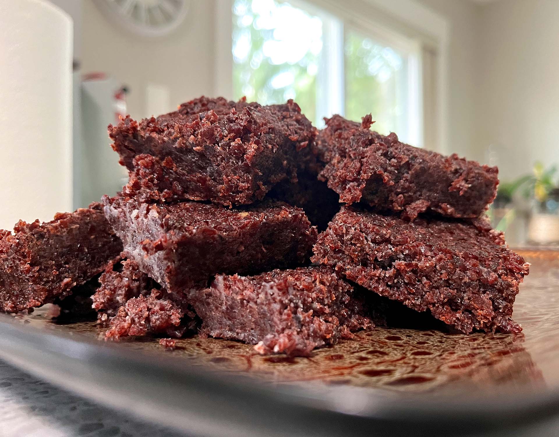 Thick rectangular pemmican bars on a wooden cutting board with a small pile of dried cranberries and a jar of rendered tallow nearby on a warm kitchen counter