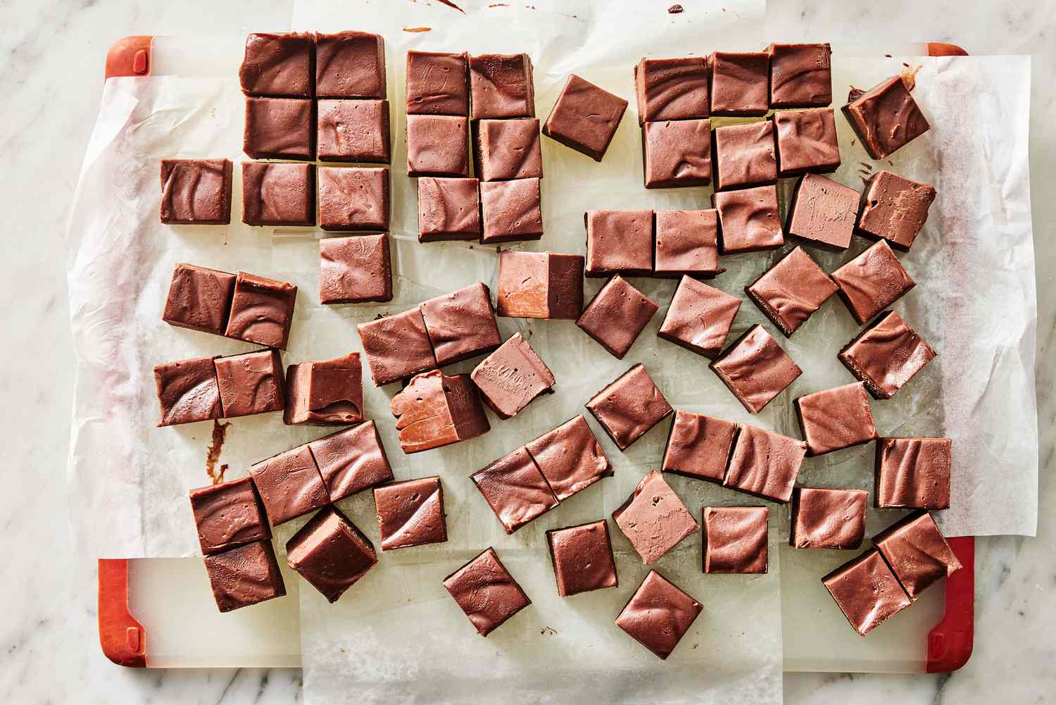 Thick squares of cocoa fudge on parchment paper on a warm-toned kitchen counter, with a small knife nearby and soft natural window light