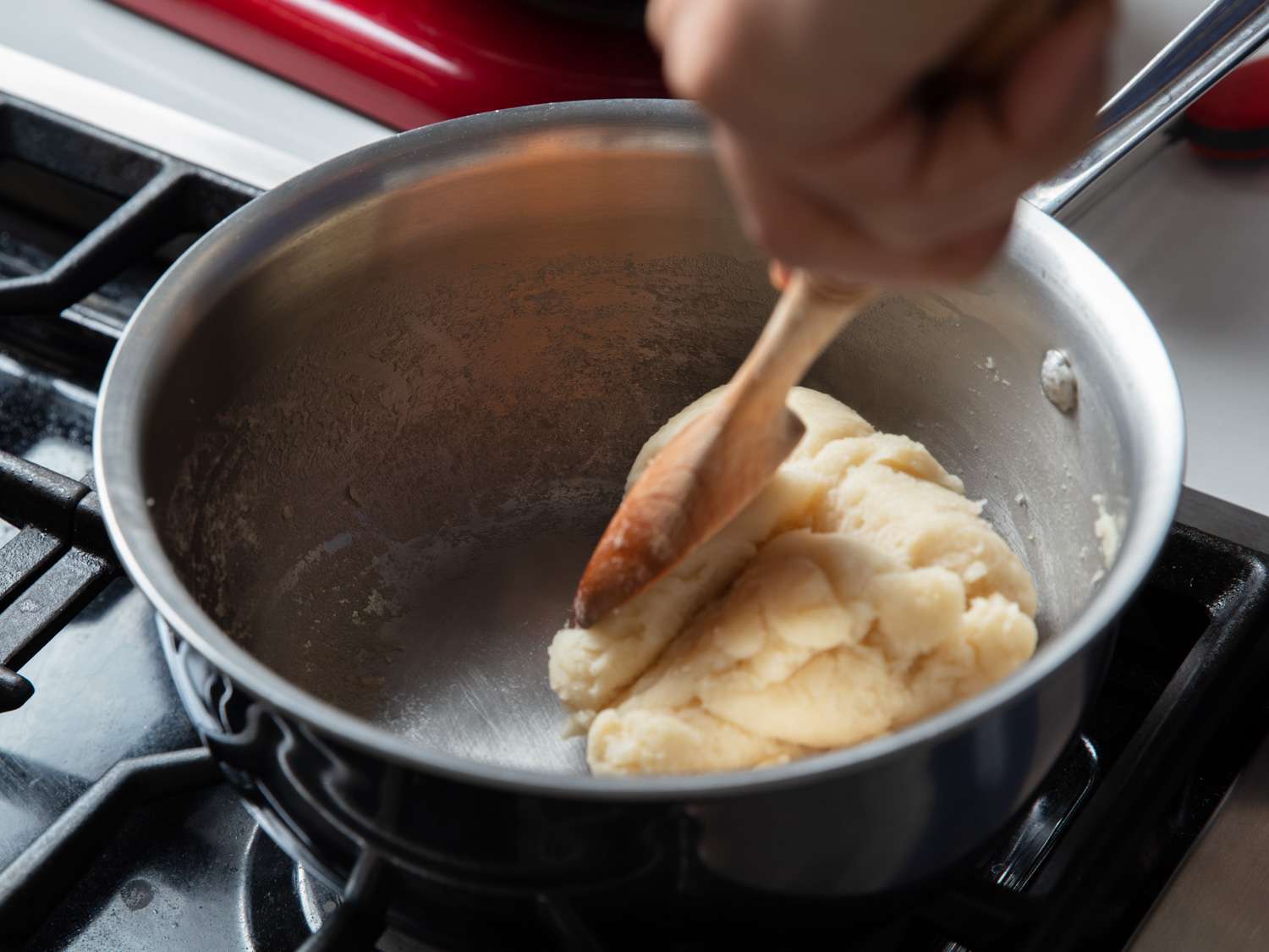 Thick zeppole dough being stirred in a saucepan as it forms a smooth ball and pulls away from the sides