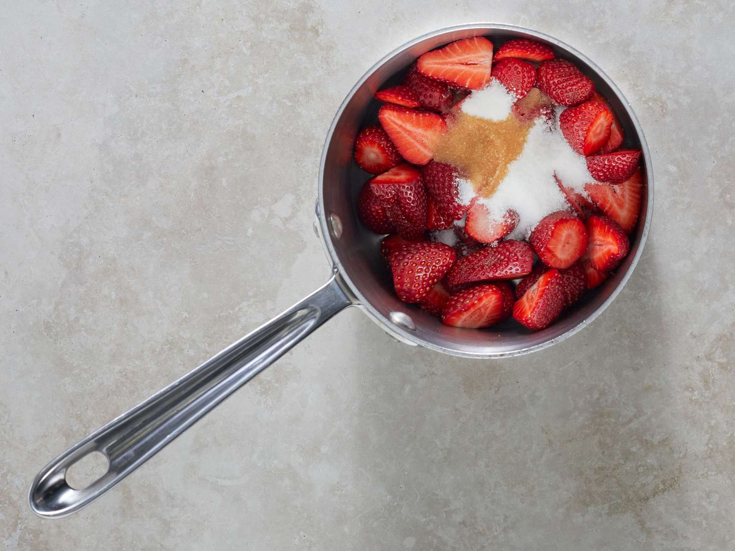 Thickened strawberry filling simmering in a small saucepan on a stovetop with a wooden spoon