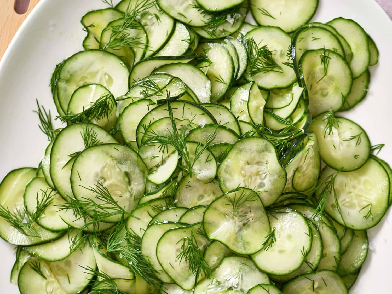 Thin cucumber slices on a cutting board lightly salted and resting with a paper towel nearby in a bright home kitchen