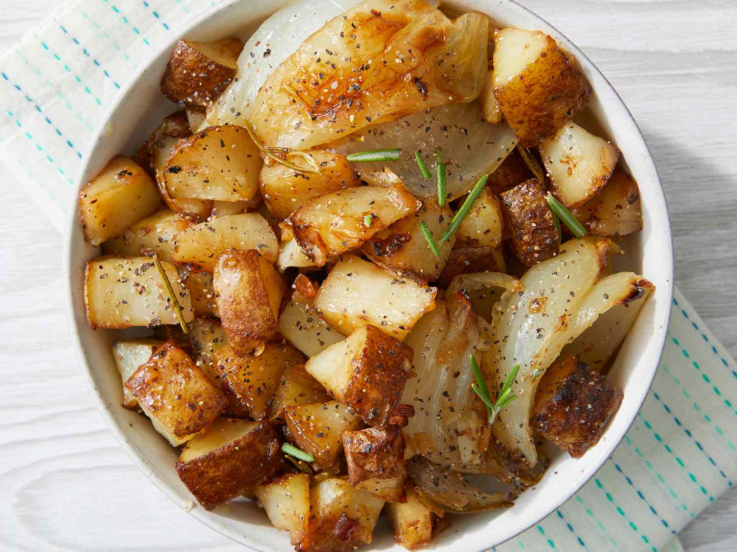 Thin potato slices and onion strands simmering gently in olive oil in a skillet, with a wooden spoon stirring