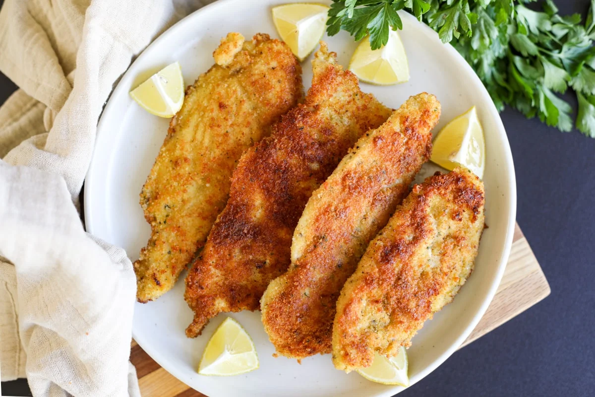 Thin slices of chicken coated in cornstarch in a mixing bowl on a kitchen counter, ready to pan-fry