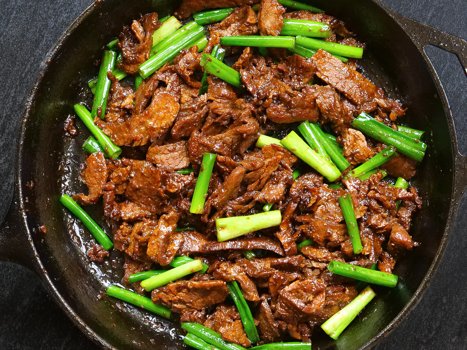 Thin slices of flank steak in a bowl being tossed with cornstarch and soy sauce using a spoon