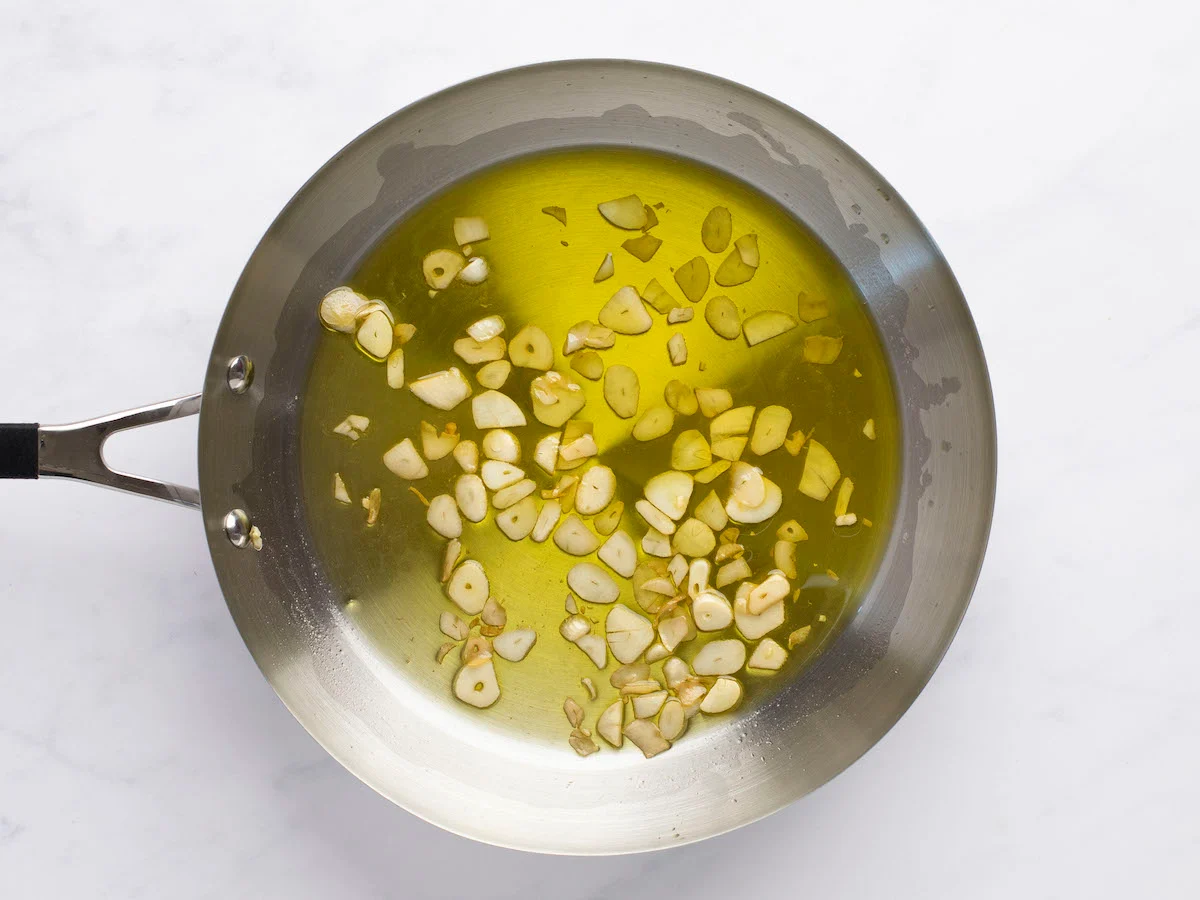 Thin slices of garlic sizzling in olive oil in a stainless steel skillet on a home stove