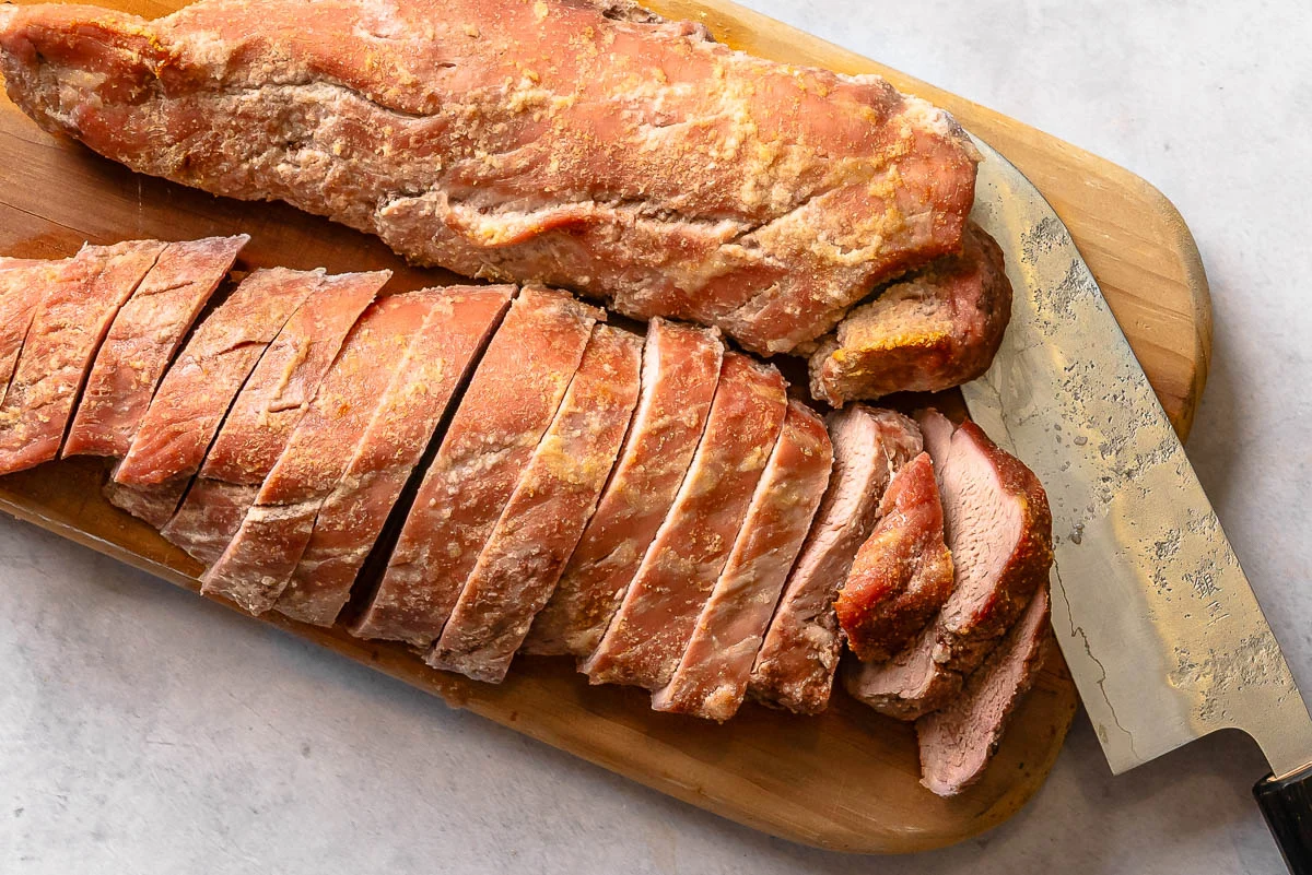 Thin slices of raw pork tenderloin fanned out on a cutting board with a chef's knife beside them