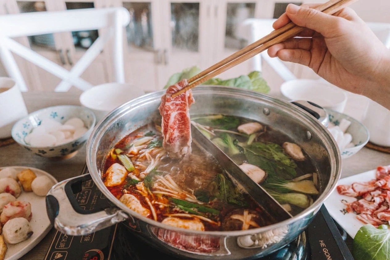 Thinly sliced beef being swished through simmering hot pot broth at the table using chopsticks
