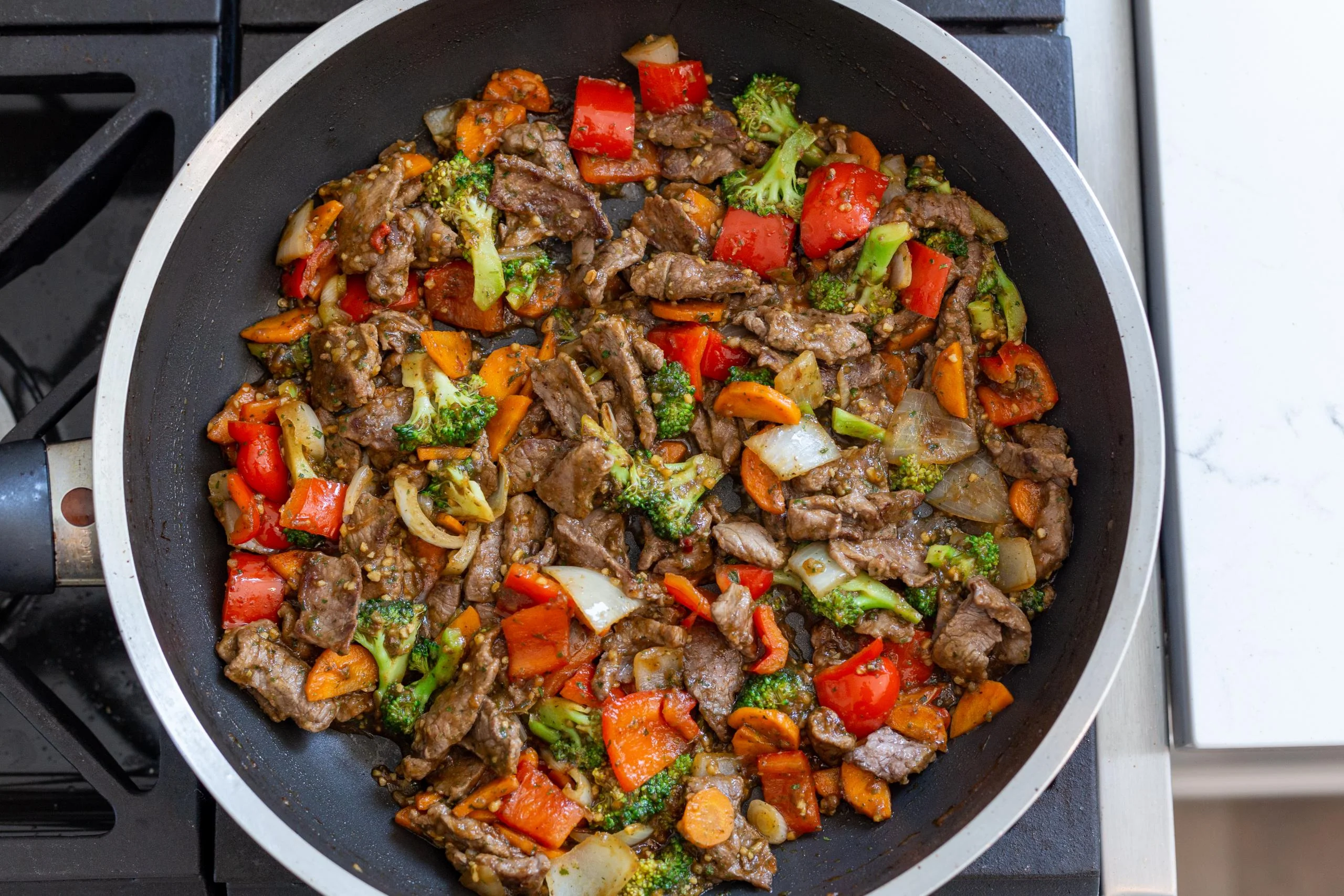 Thinly sliced beef searing in a hot skillet with browned edges and steam rising under kitchen lighting