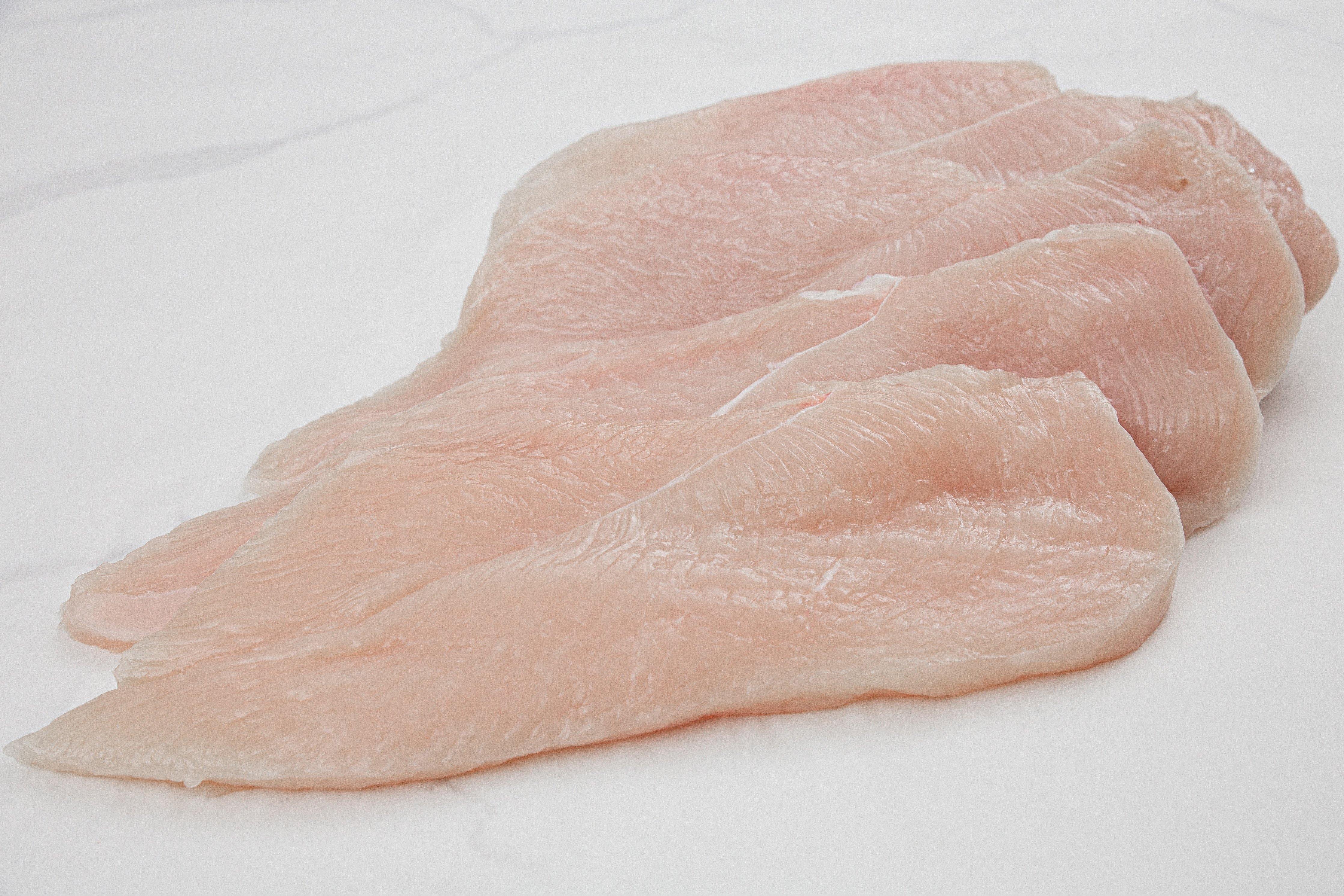 Thinly sliced chicken breast strips on a cutting board with a chef's knife beside them
