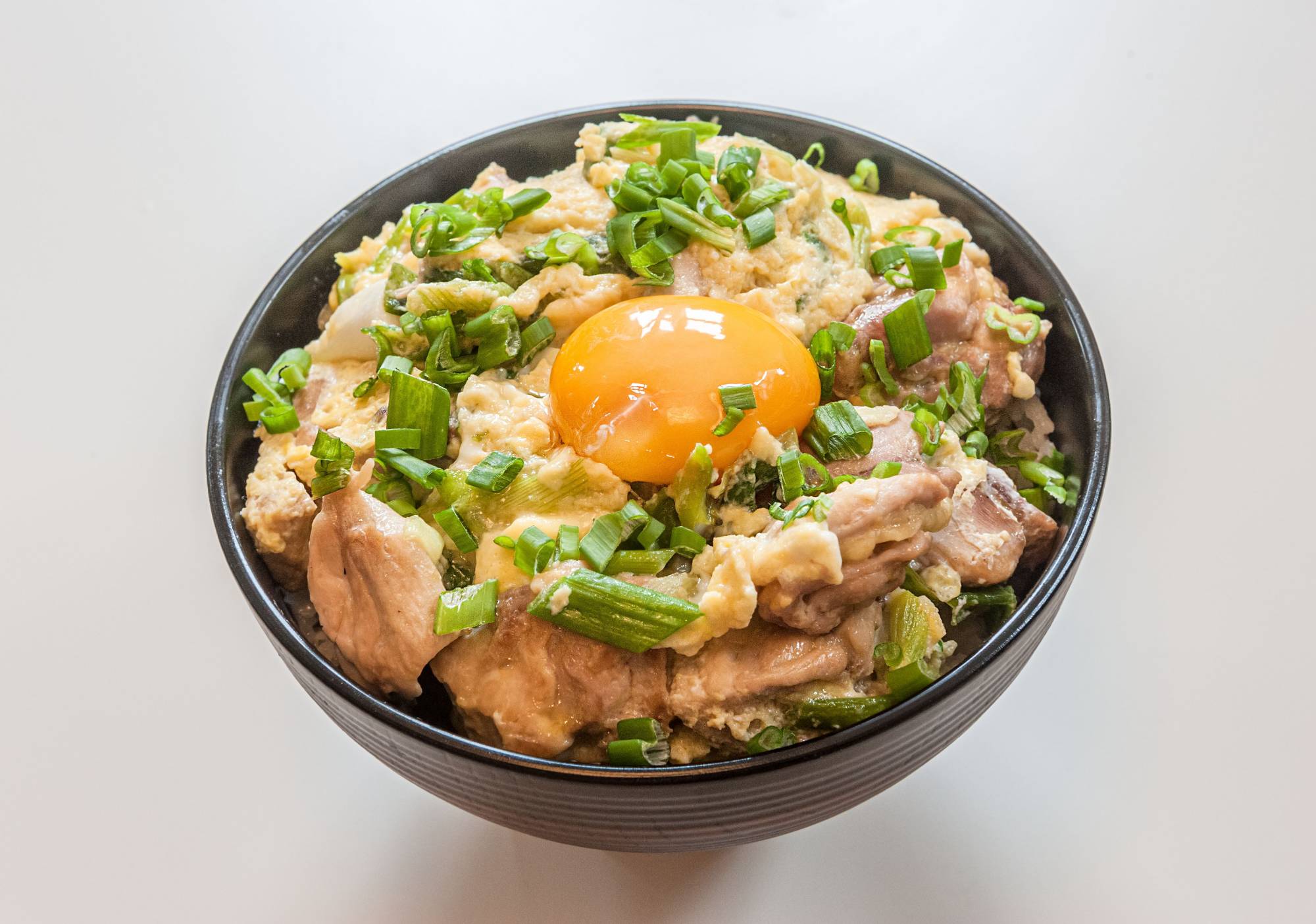Thinly sliced chicken thighs and onions prepped beside a bowl of lightly beaten eggs on a kitchen counter