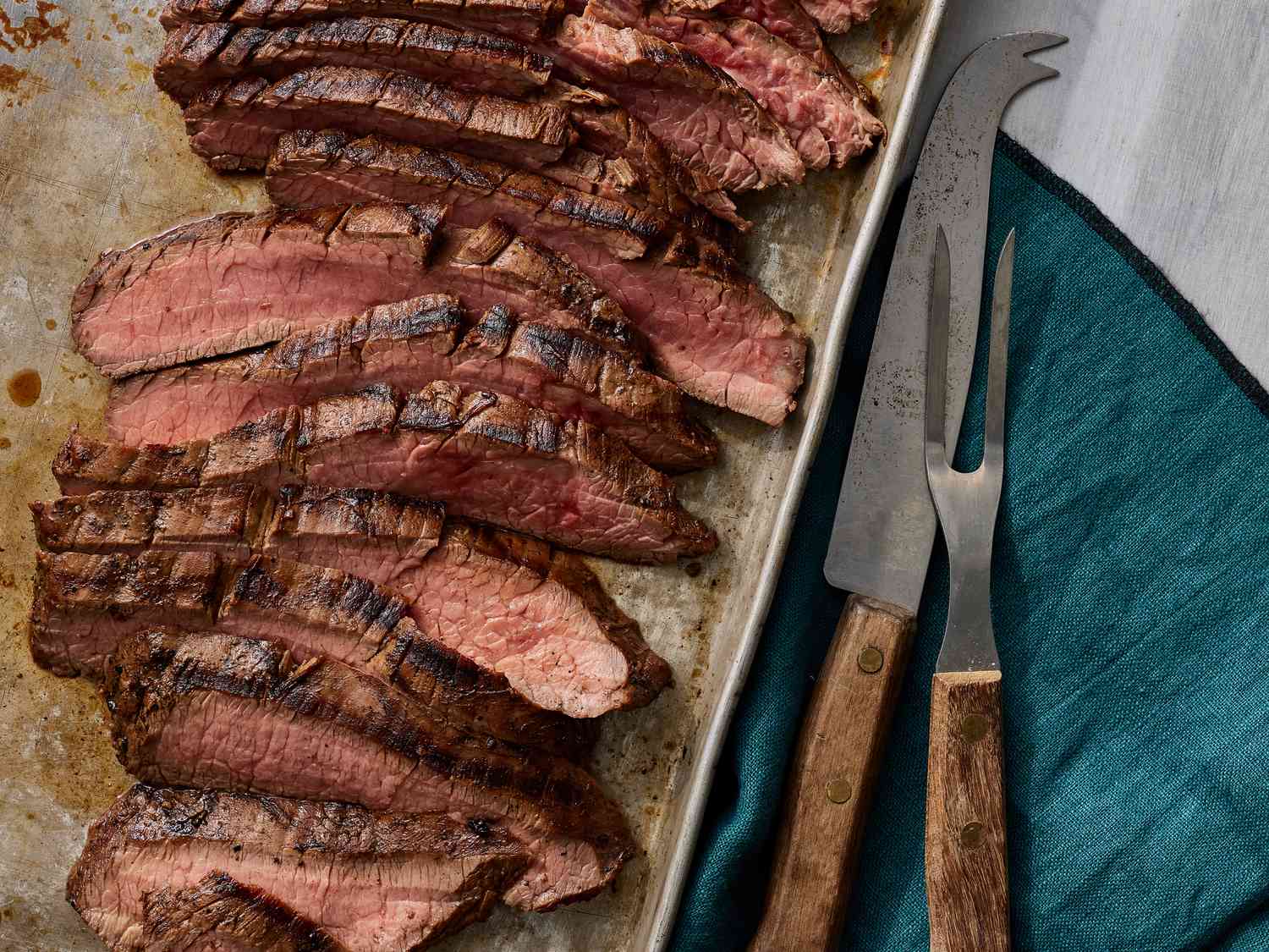 Thinly sliced flank steak on a wooden cutting board with visible grain direction, next to a chef’s knife