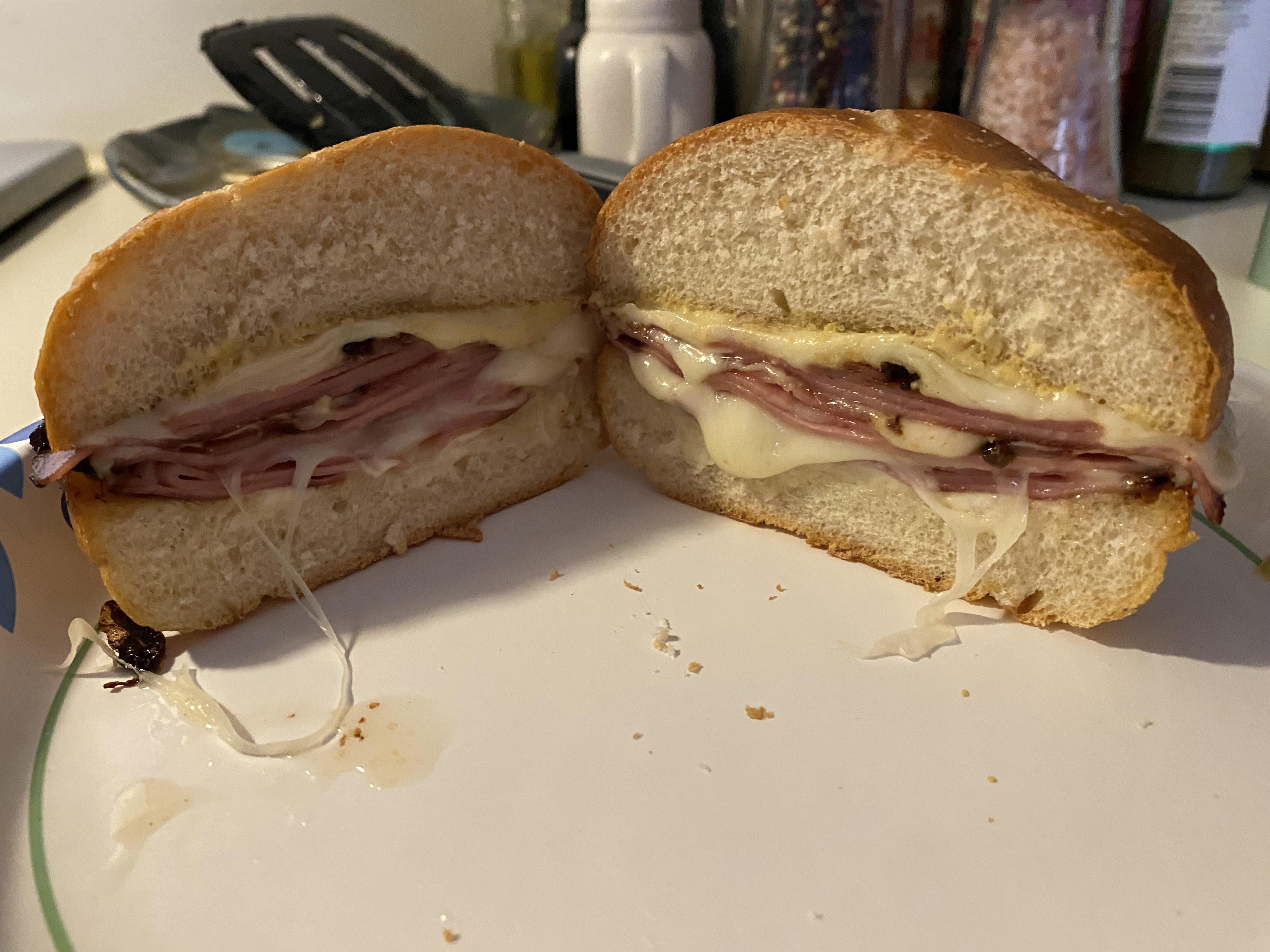 Thinly sliced mortadella, slices of provolone, a kaiser roll, mustard, mayonnaise, and a small bottle of neutral oil arranged on a clean kitchen counter