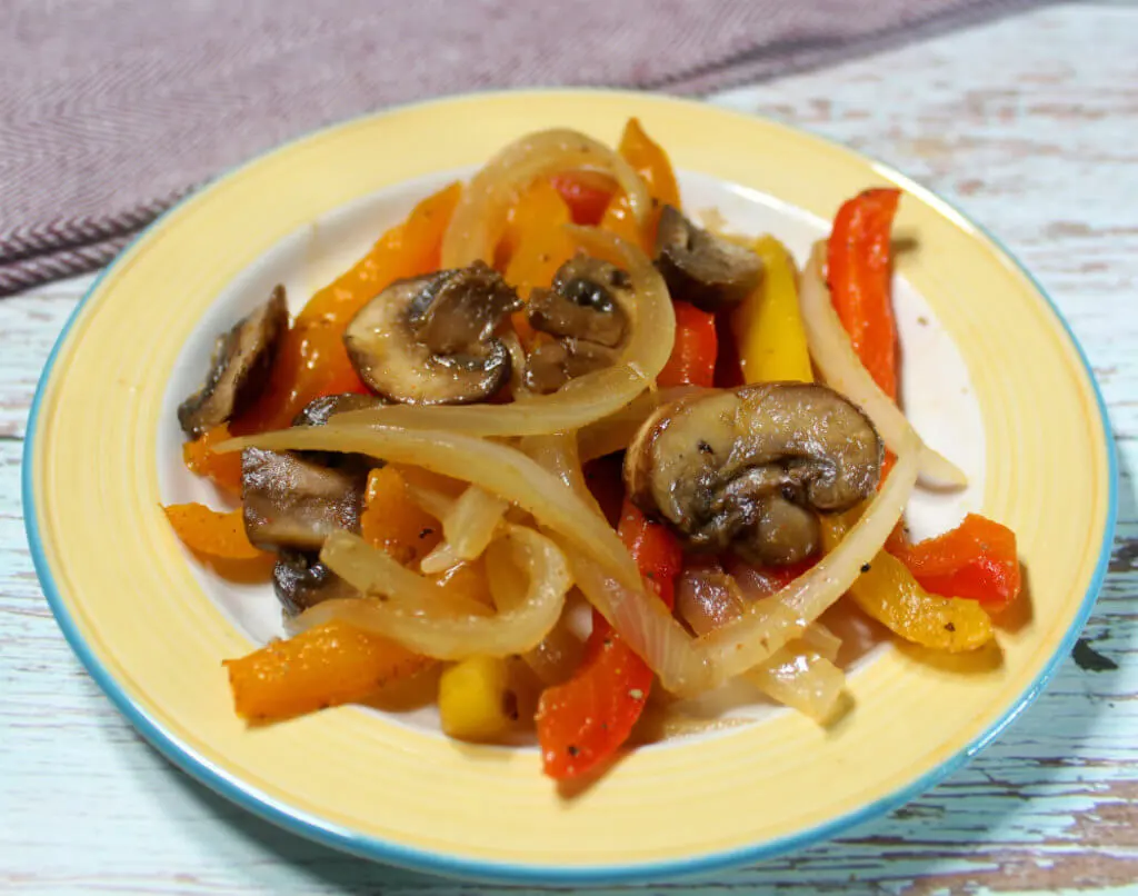 Thinly sliced mushrooms, bell peppers, and red onion arranged on a wooden cutting board next to a knife on a kitchen counter