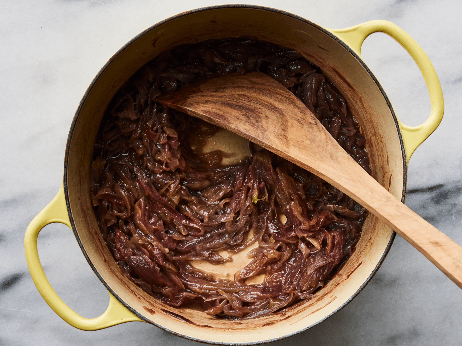 Thinly sliced onions slowly cooking down in a heavy pot on a stovetop, turning soft and golden-brown