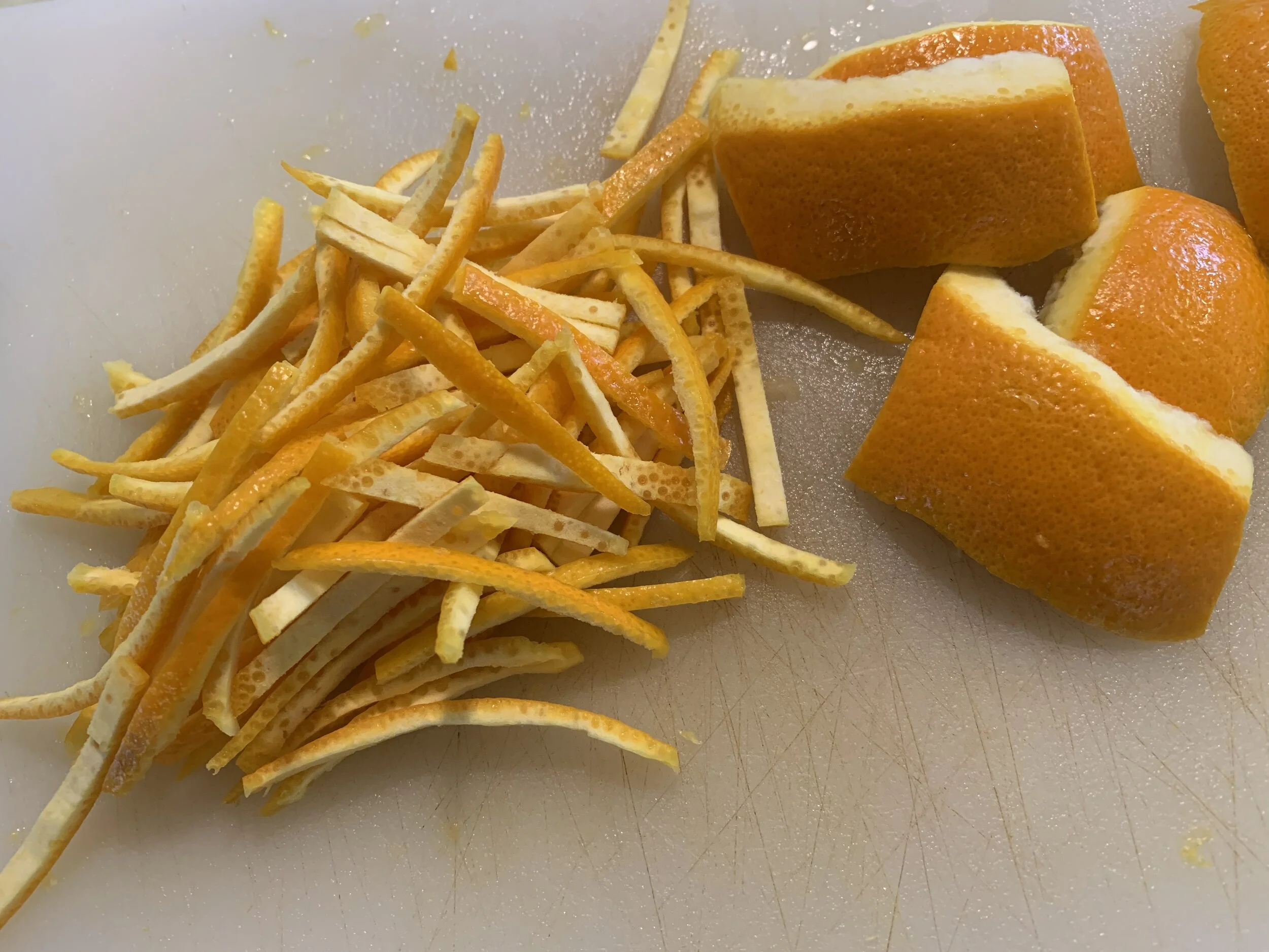 Thinly sliced orange peel matchsticks and chopped citrus on a cutting board with a knife, ready to cook