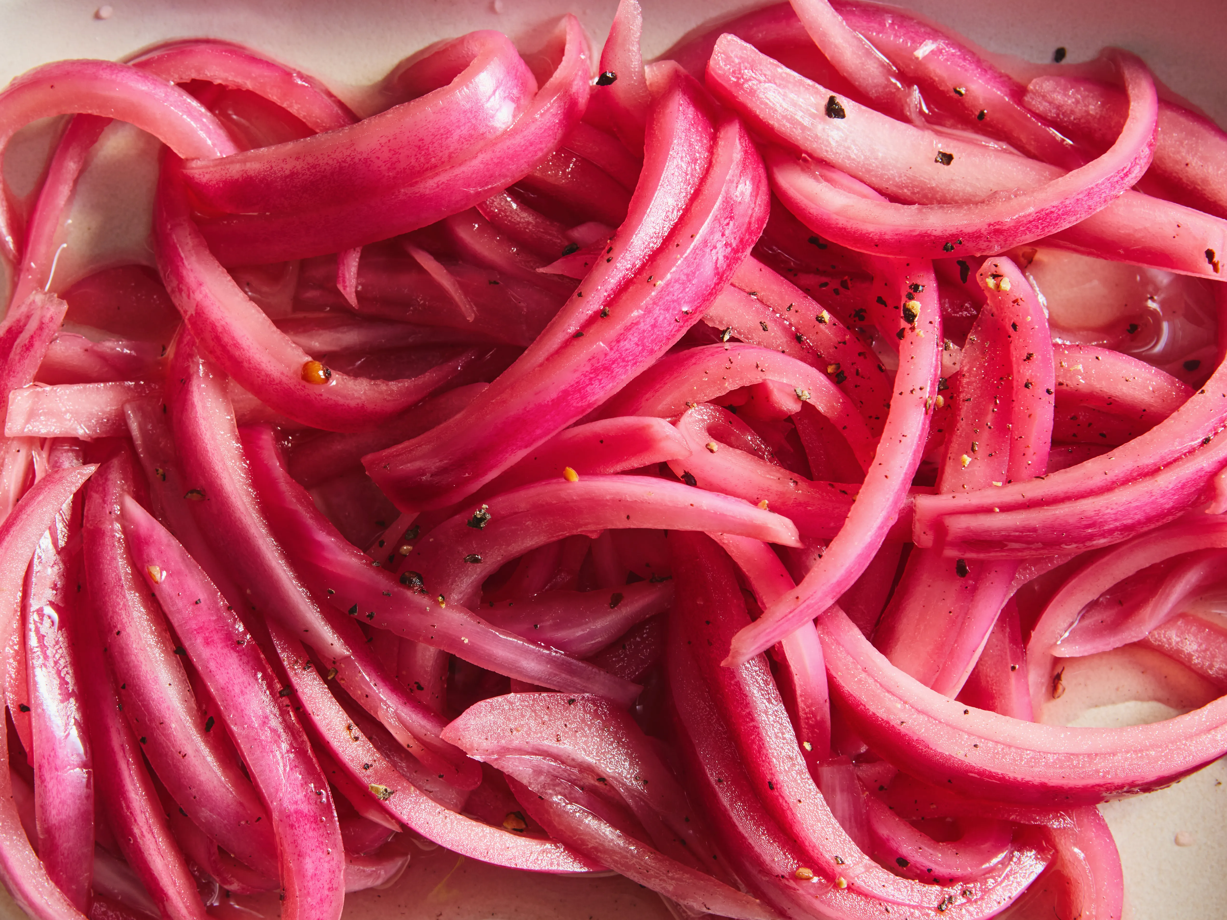 Thinly sliced red onion rings piled on a wooden cutting board beside a chef’s knife on a home kitchen counter