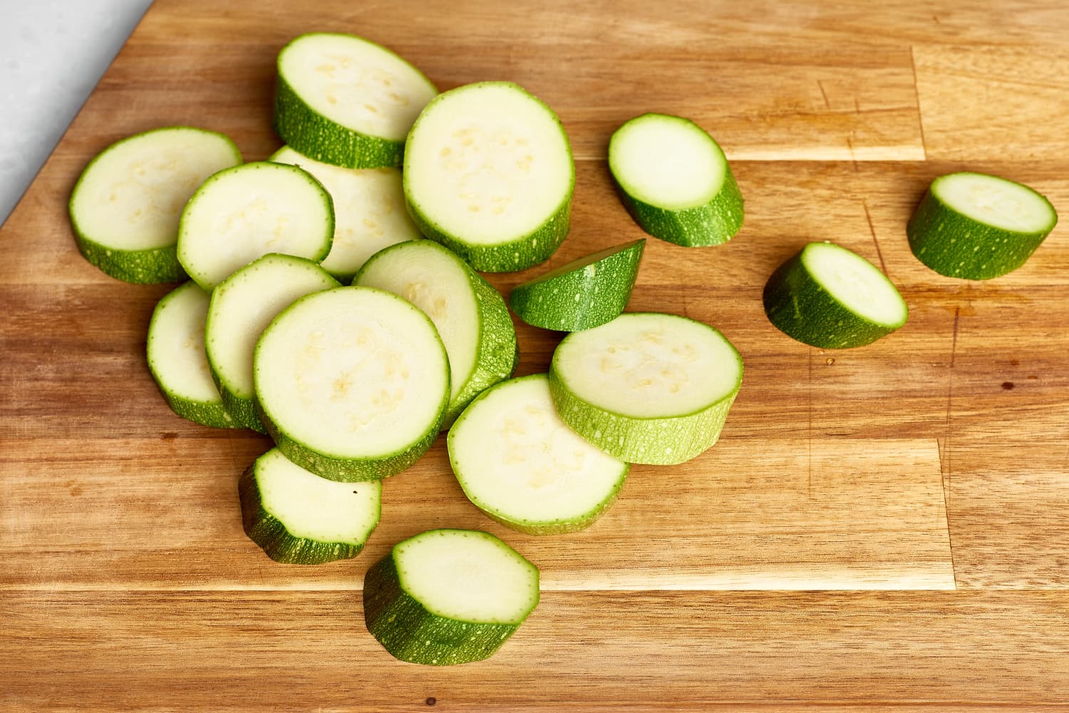 Thinly sliced zucchini half-moons on a wooden cutting board beside a chef’s knife on a bright kitchen counter