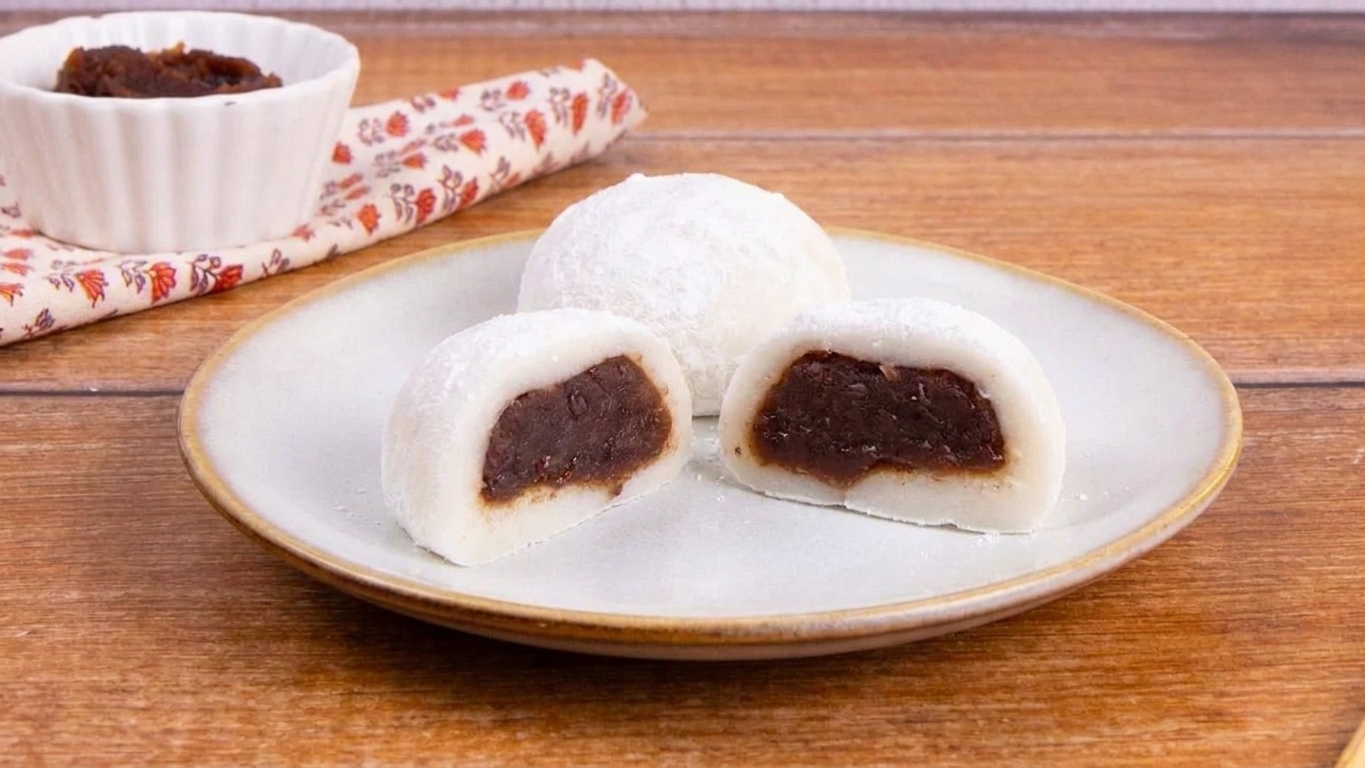 Three filled mochi balls dusted with starch on a small ceramic plate on a wooden table