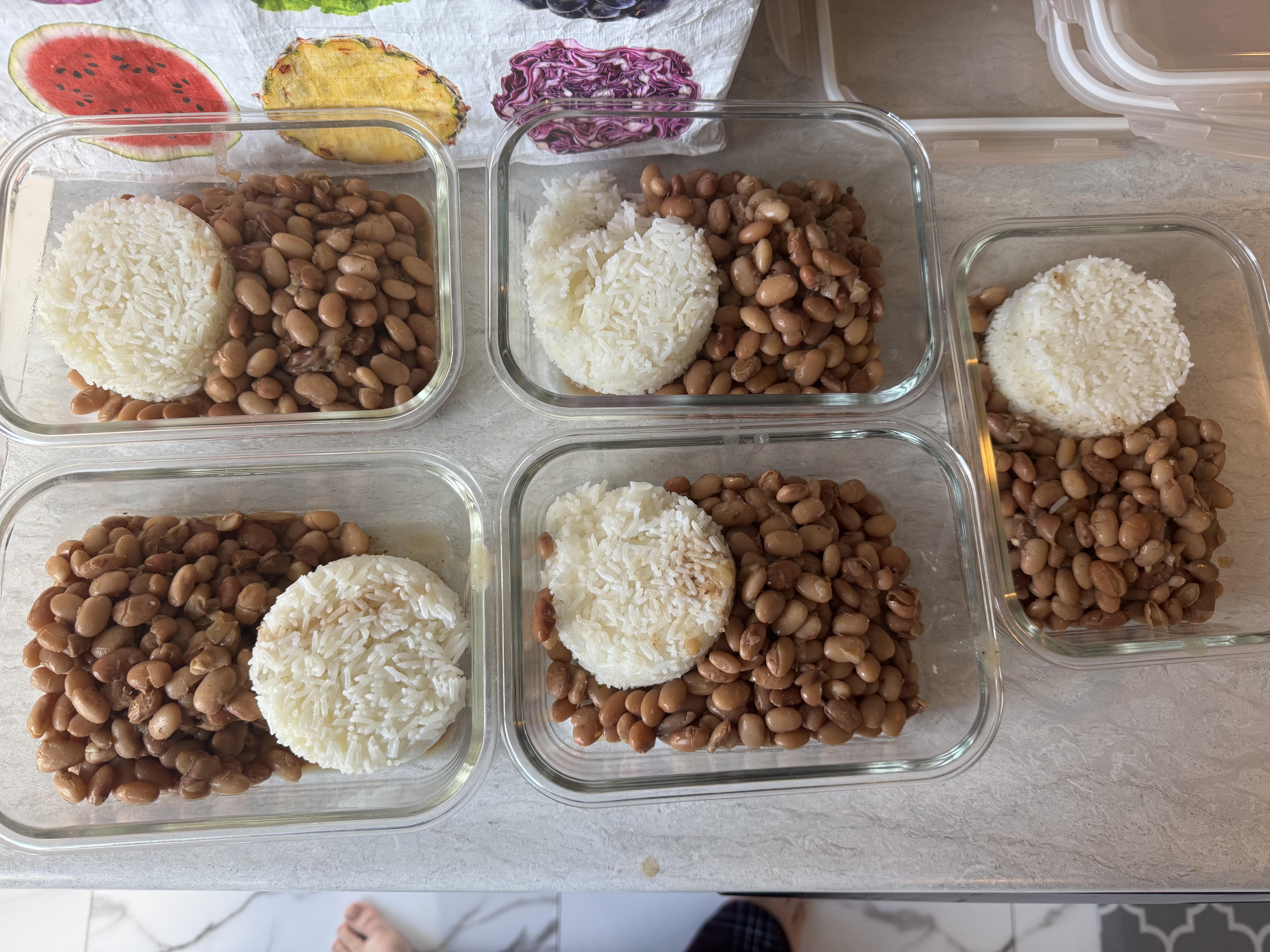 Three glass meal prep containers filled with white rice, red beans, and stewed chicken on a kitchen counter