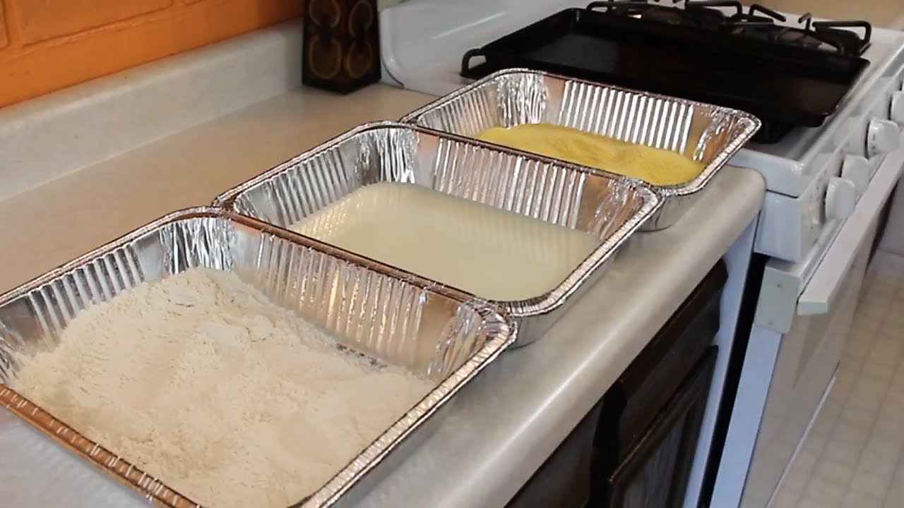 Three shallow bowls on a kitchen counter set up for dredging chicken with flour, beaten eggs, and breadcrumb Parmesan mixture