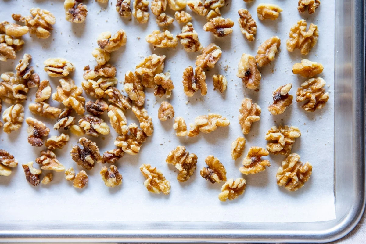 Toasted walnut pieces spread on a metal baking sheet, lightly browned and fragrant-looking, close-up food photography