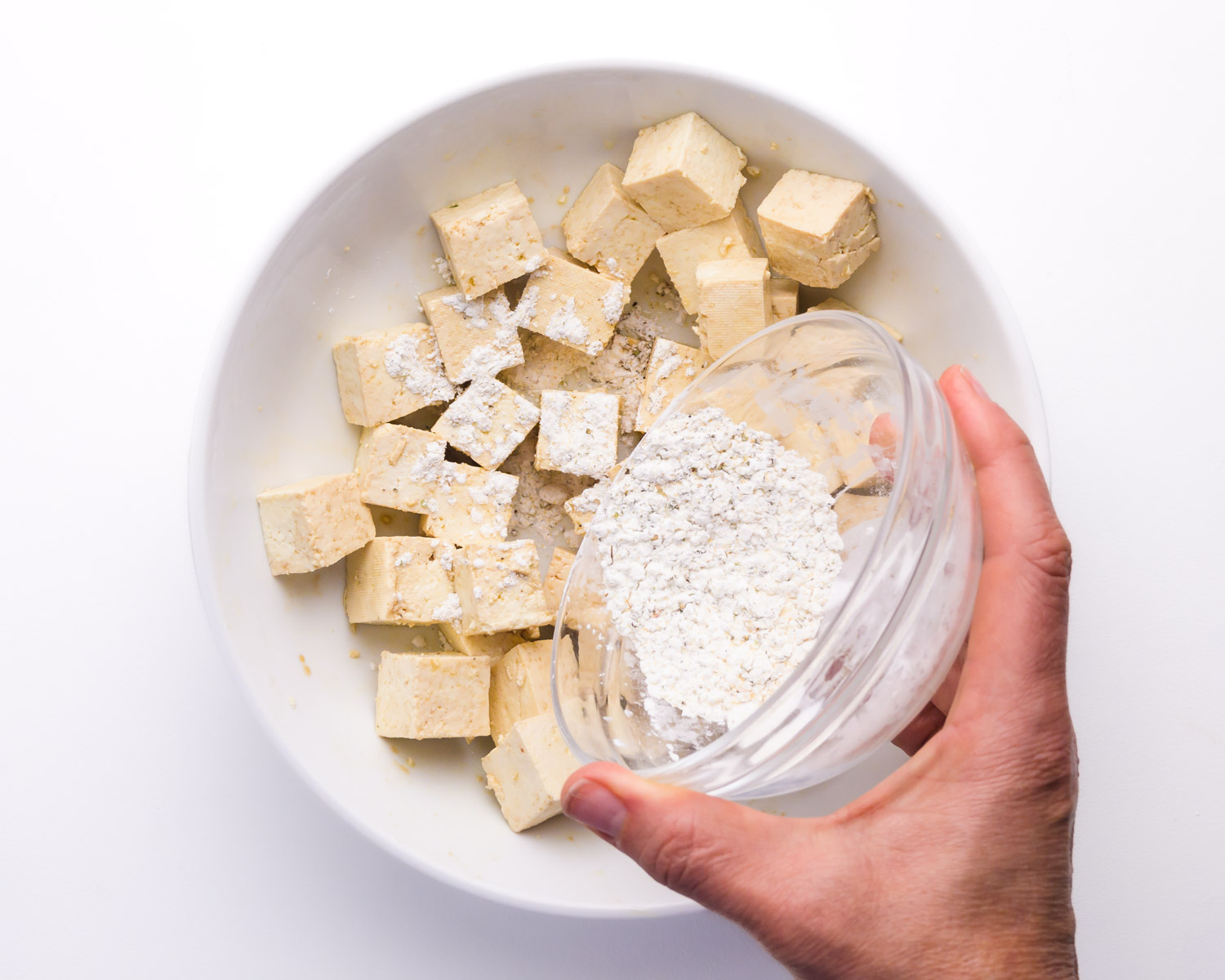 Tofu cubes being tossed in cornstarch in a mixing bowl on a bright kitchen counter