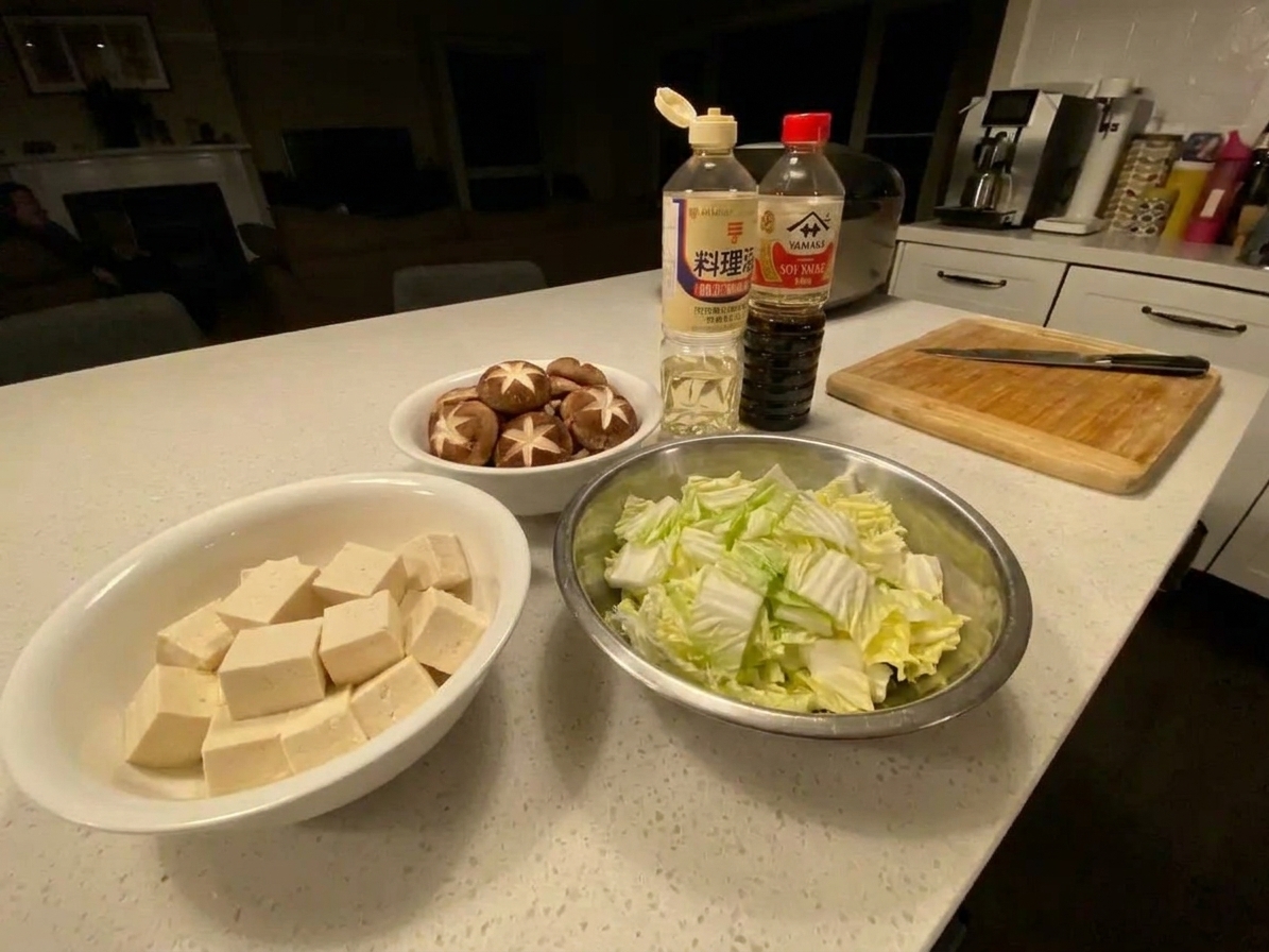 Tofu cubes, sliced shiitake mushrooms, and sliced napa cabbage arranged in separate bowls on a kitchen counter, ready for sukiyaki