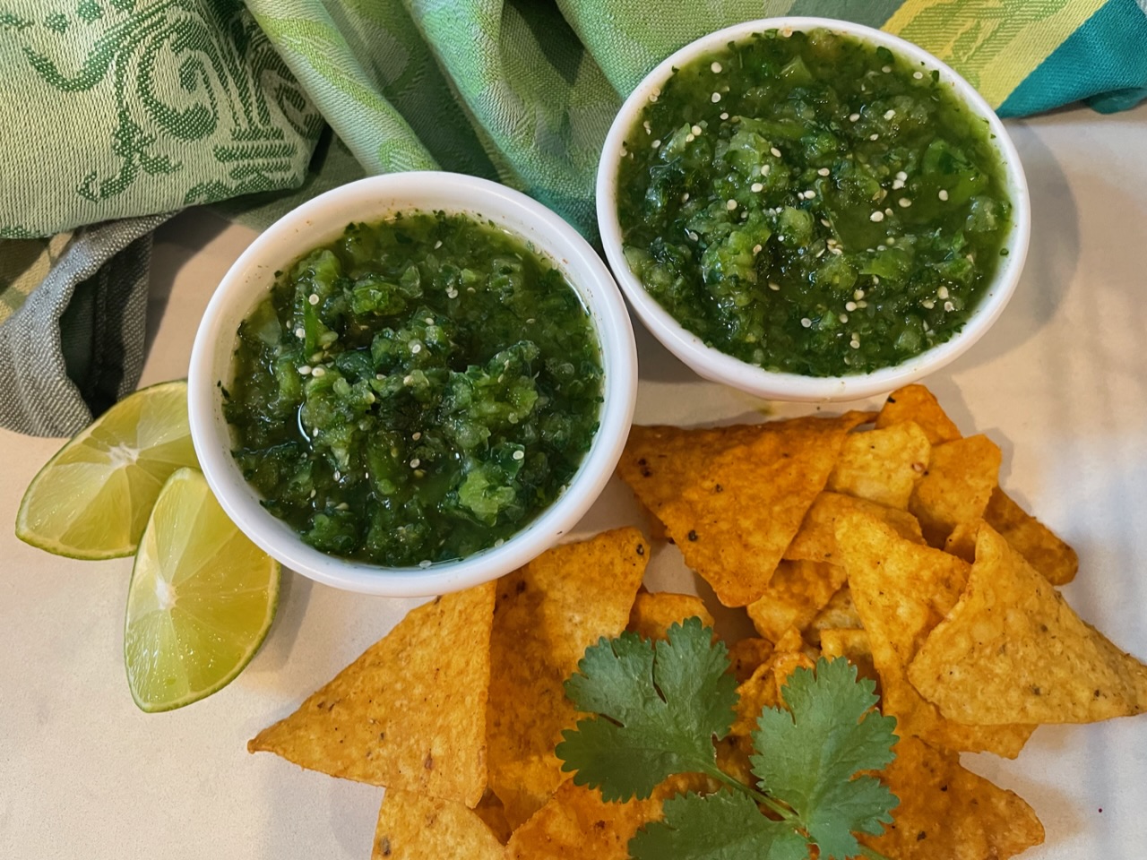 Tomatillos, jalapeno, garlic, cilantro, lime, onion, and spices arranged on a wooden cutting board in a home kitchen