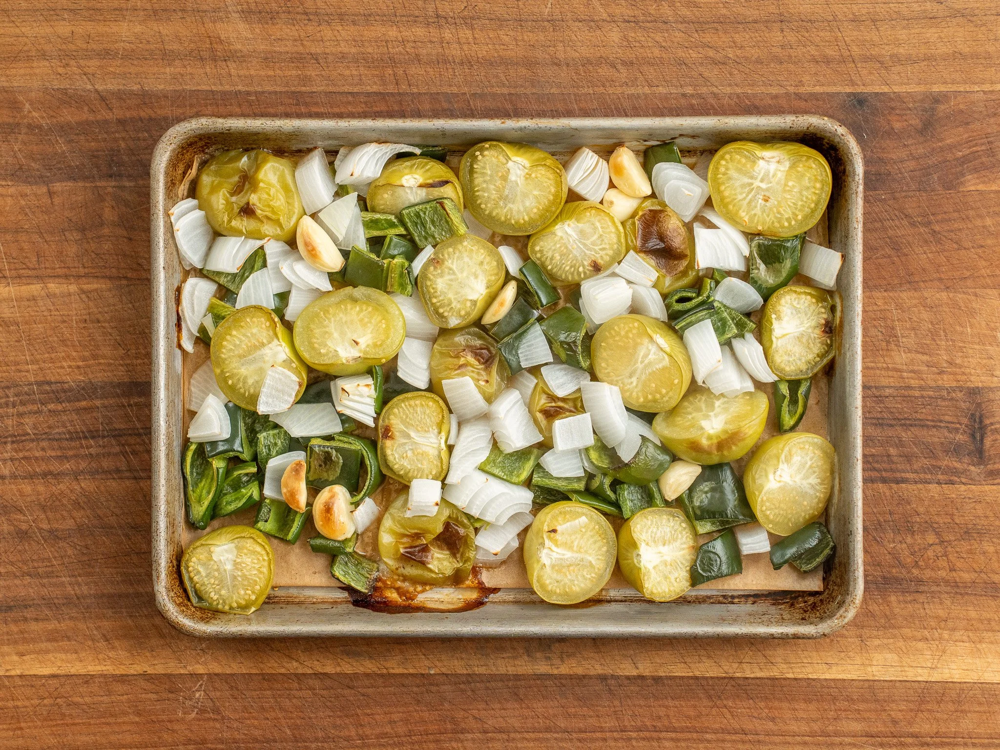 Tomatillos, jalapeño, onion wedges, and garlic cloves spread on a foil-lined sheet pan before roasting in a home kitchen