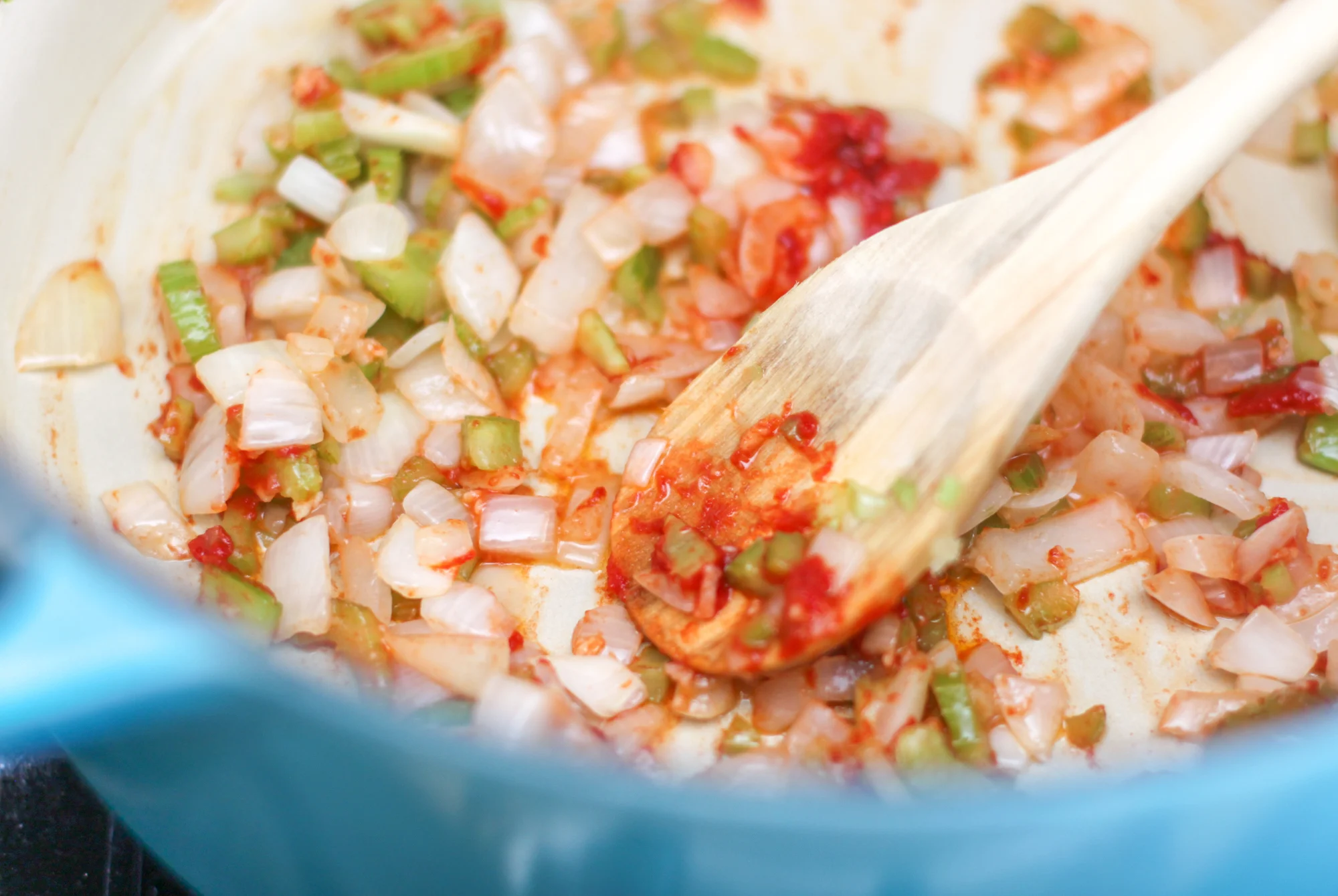 Tomato paste being stirred into sauteed onions and garlic in a large pot on the stovetop with a wooden spoon