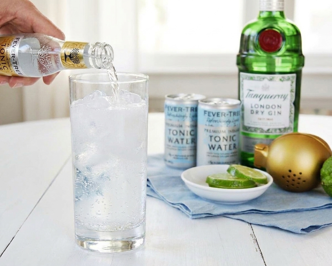 Tonic water being poured from a small bottle into a highball glass with gin and ice